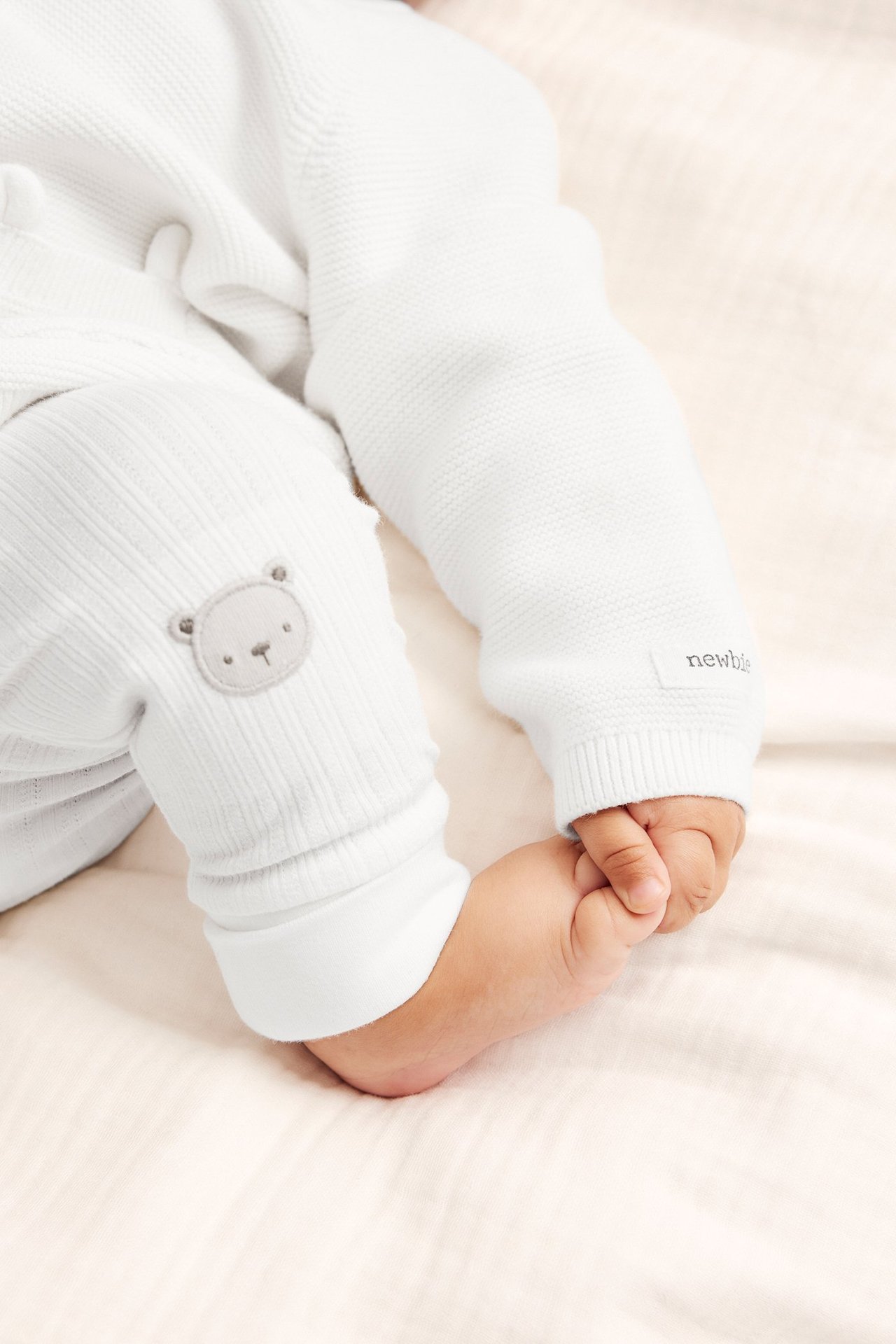 Close-up of baby wearing off-white ribbed jersey leggings with a bear application and an off-white knitted top.