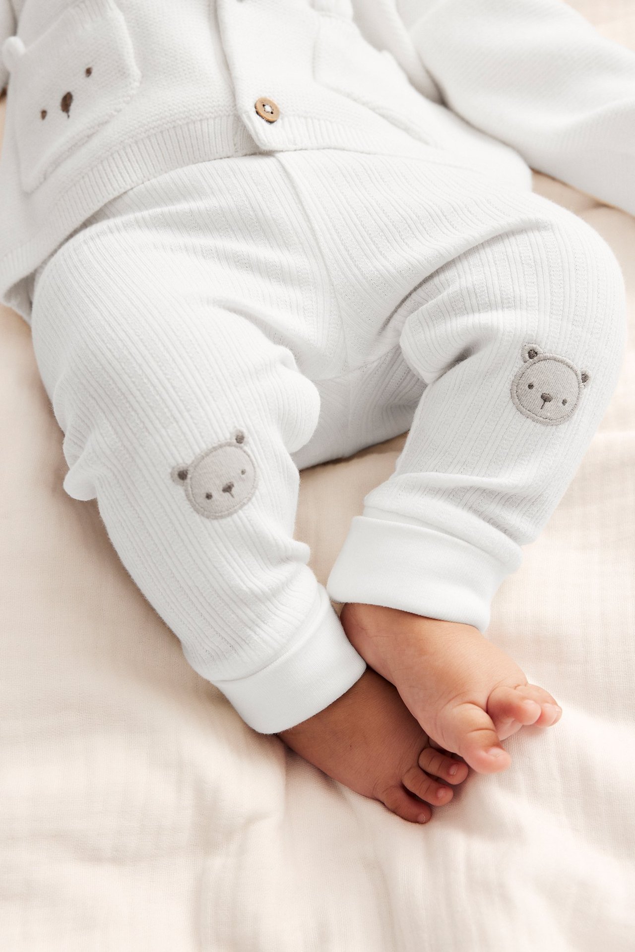 Close-up of baby wearing off-white ribbed jersey leggings with bear appliques and a matching cardigan.