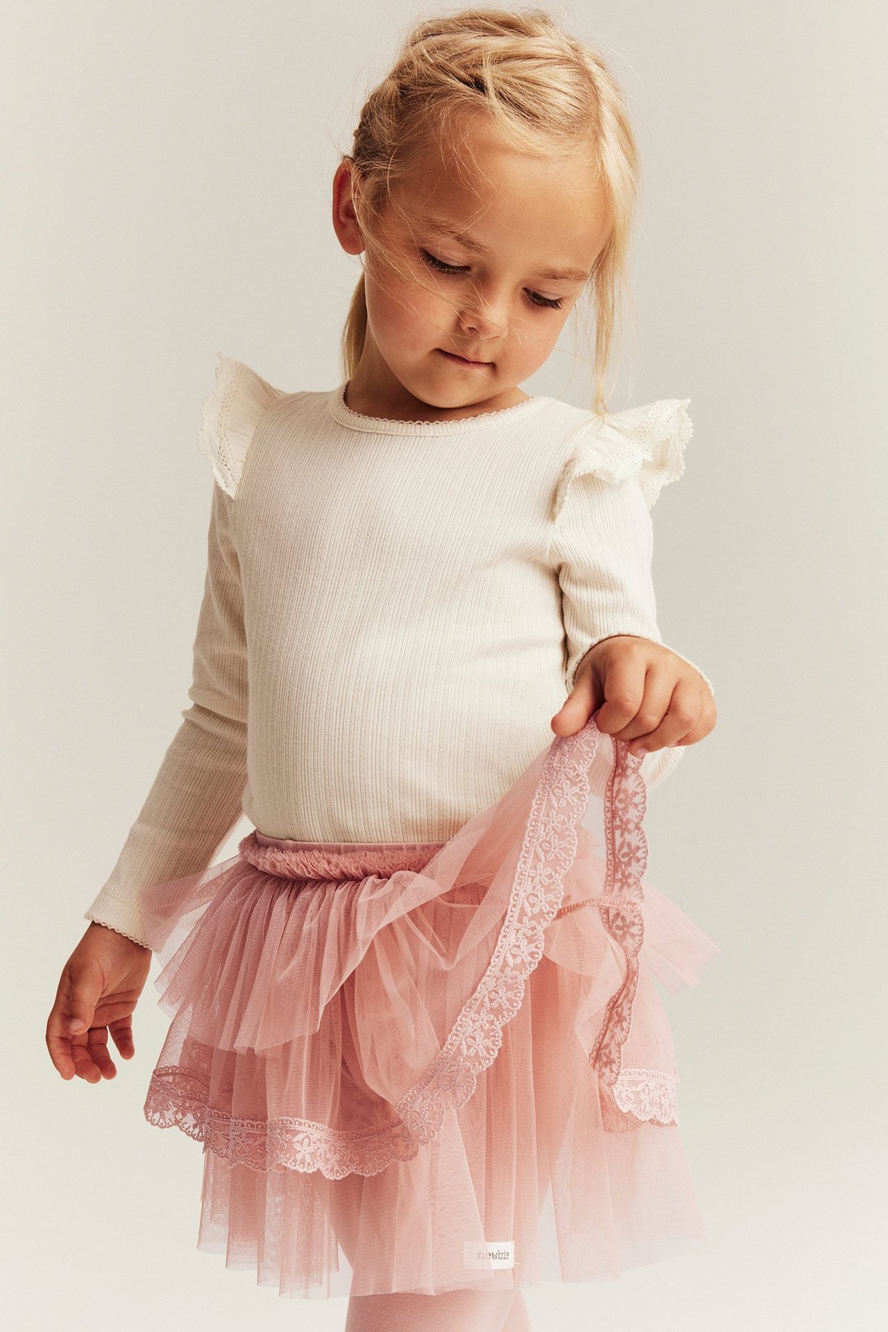 Front view of a kid wearing pink leggings with a tiered tulle skirt and a cream ribbed long-sleeved top.