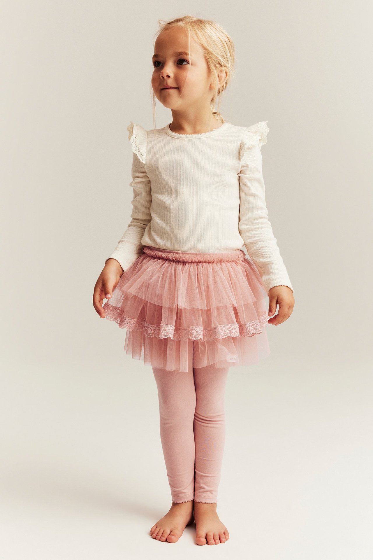 Front view of a kid wearing pink leggings with a three-tiered tulle skirt and a cream ribbed long-sleeve top.
