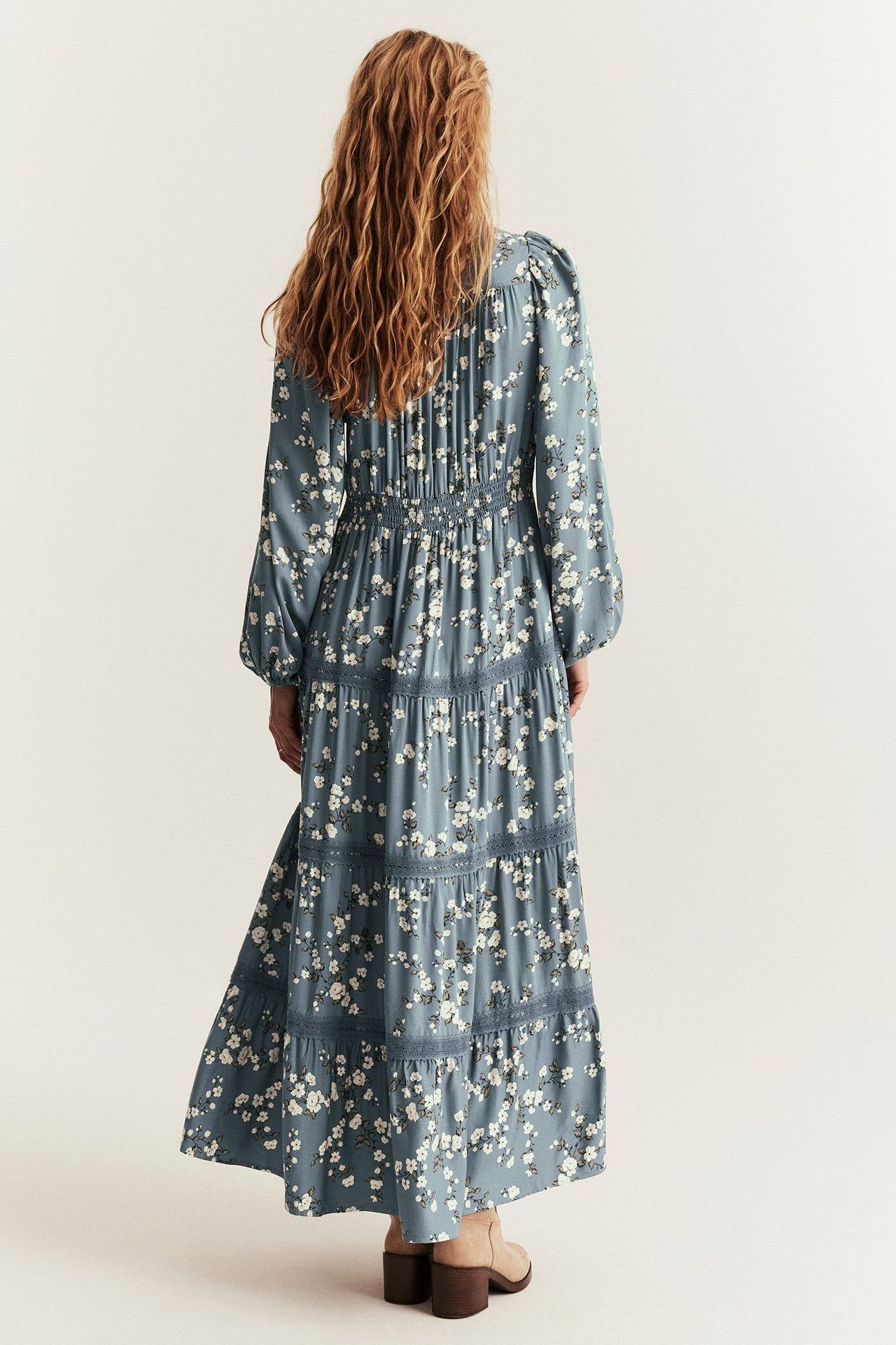 Rückenansicht einer Frau in langem blauem Blumen-Viskosekleid mit Stufenrock, Spitzendetails und Puffärmeln.