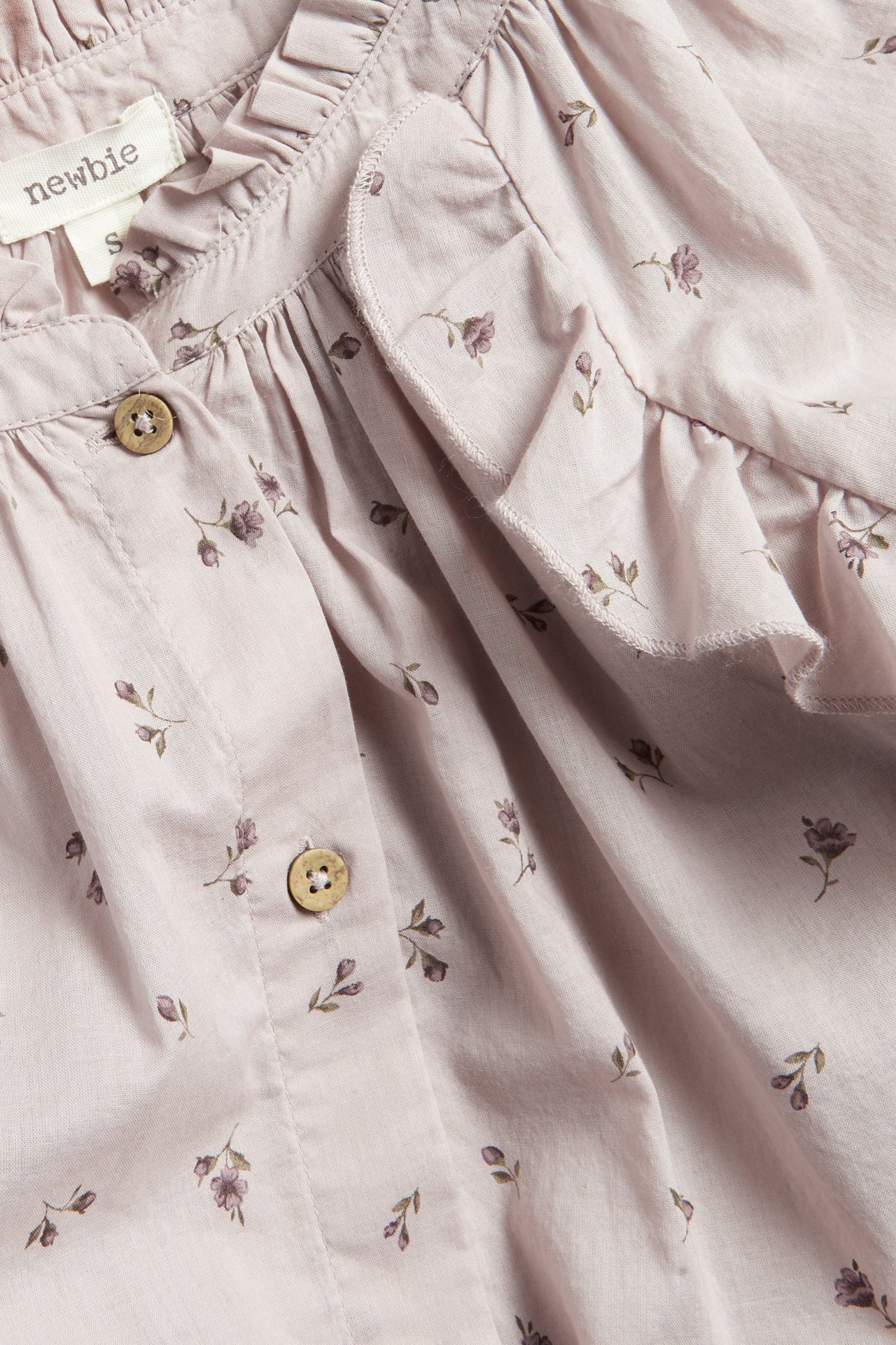 Close-up of a woman's light lilac cotton blouse with small floral print, ruffles, and wooden buttons.