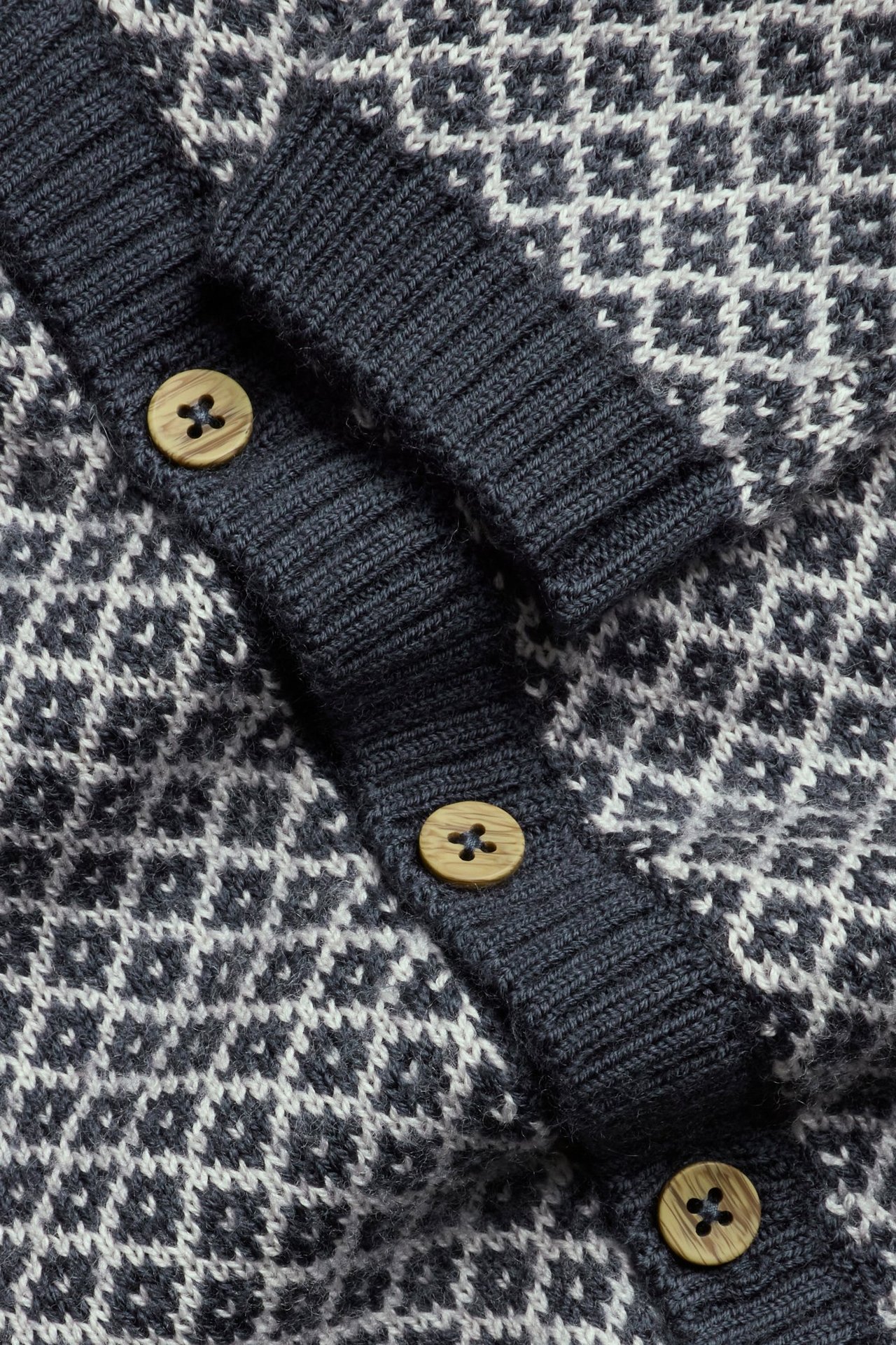 Nahaufnahme einer dunkelblauen und weißen gemusterten Wollstrickjacke mit gerippter Knopfleiste und Holzknöpfen.