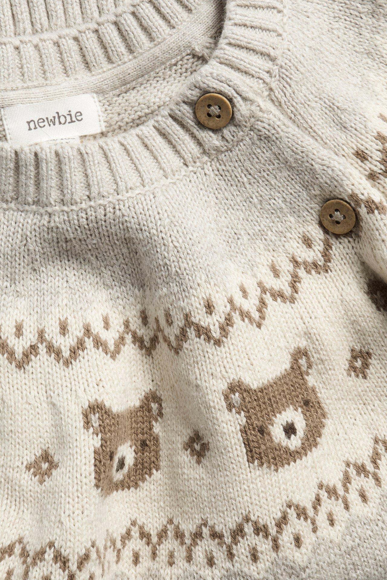 Nahaufnahme eines beigefarbenen Baby-Jacquardstrickpullovers aus Baumwolle mit braunem Bärenmuster und Schulterknöpfen.