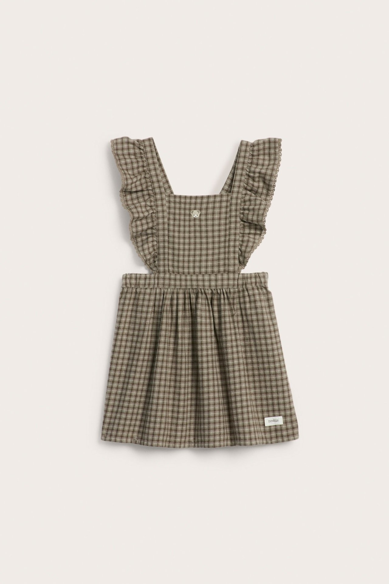 Front view of a kid's brown checked cotton pinafore dress with ruffled lace-trimmed straps and an embroidered bear.