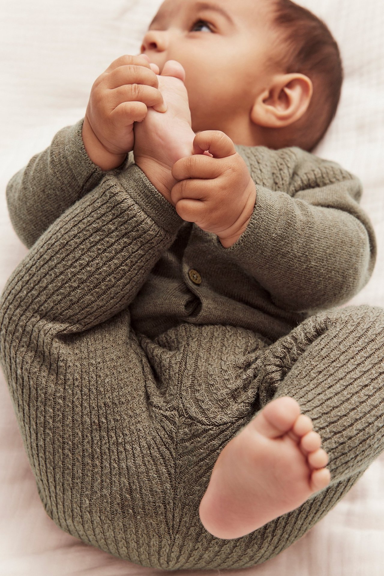 Close-up of a baby wearing olive green structured knit leggings and a matching buttoned top.