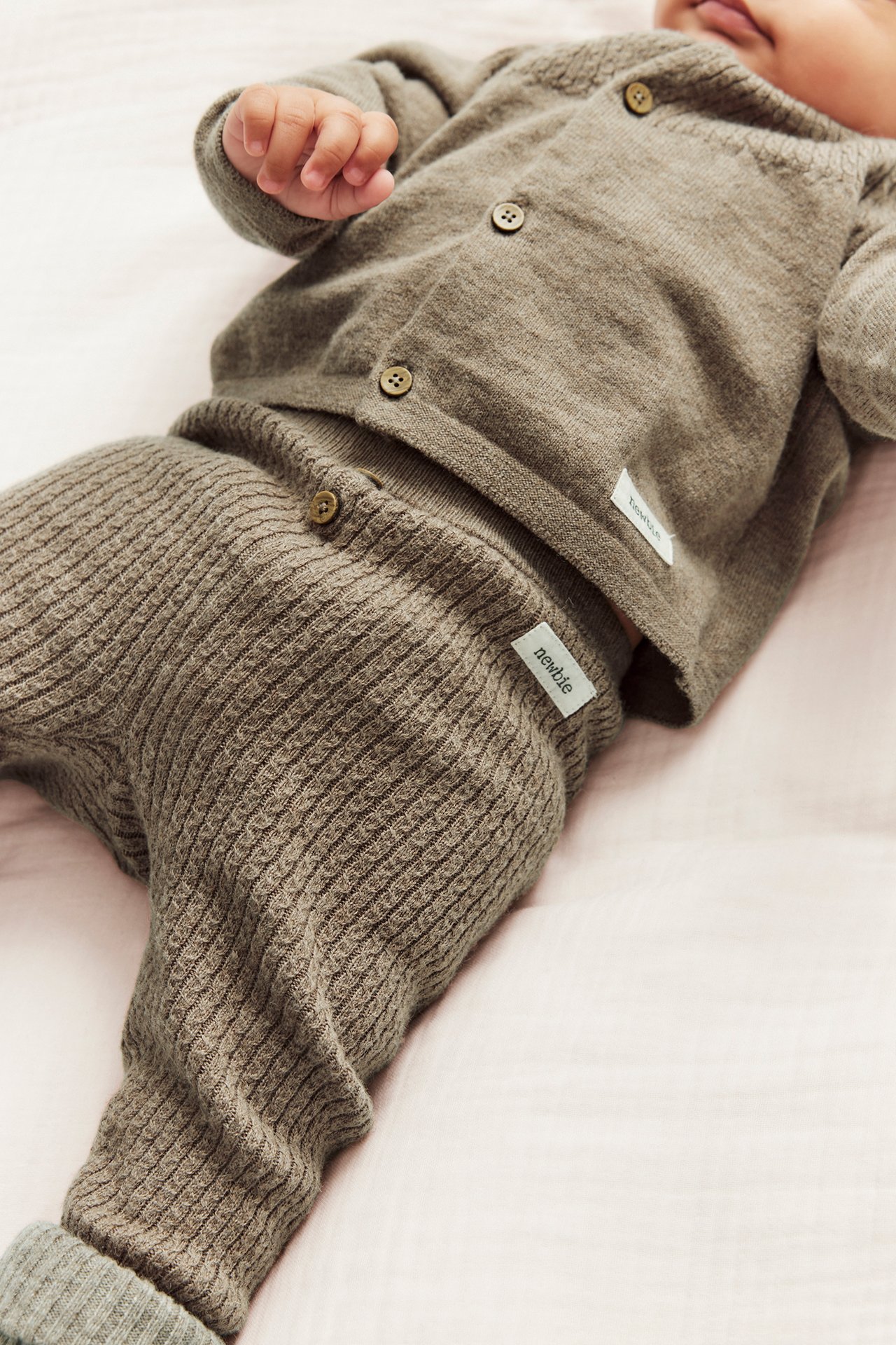 Close-up of a baby wearing brown melange structured knit wool/cotton leggings with decorative buttons and a matching cardigan.