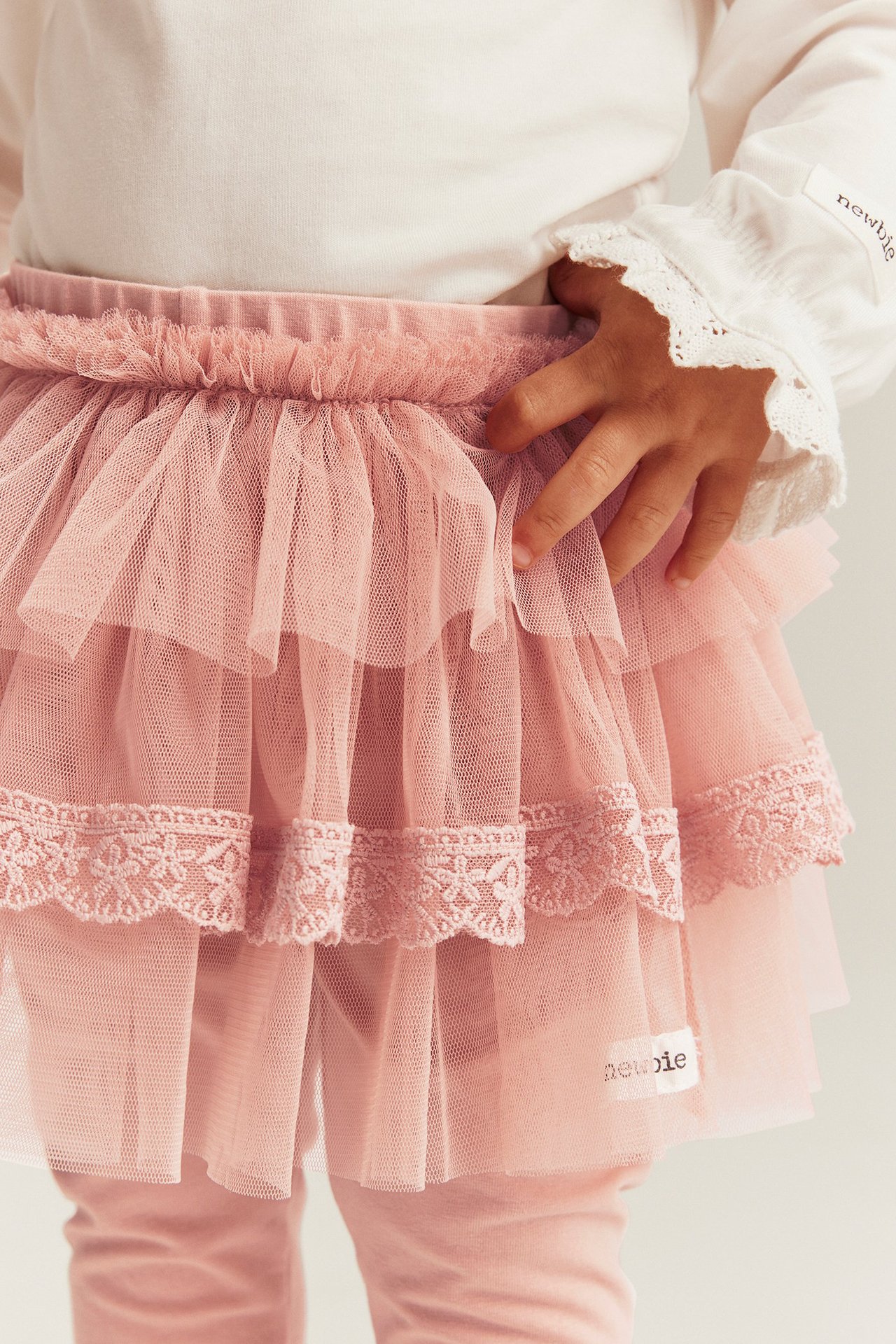 Nahaufnahme von rosa Leggings mit angenähtem gestuftem Tüllrock, getragen von einem Baby mit weißem Langarmshirt.