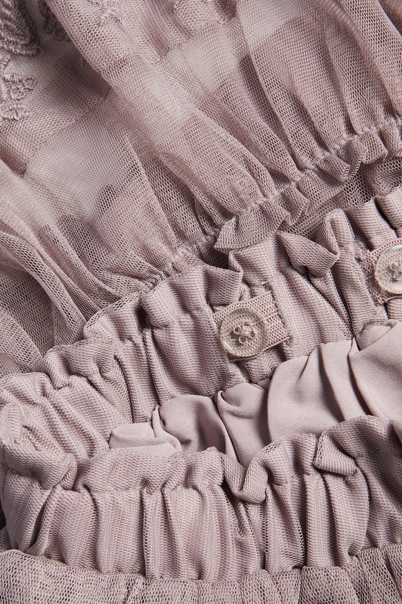 Close-up of a light lilac mesh skirt with embroidered ruffles and adjustable elastic waist with buttons.