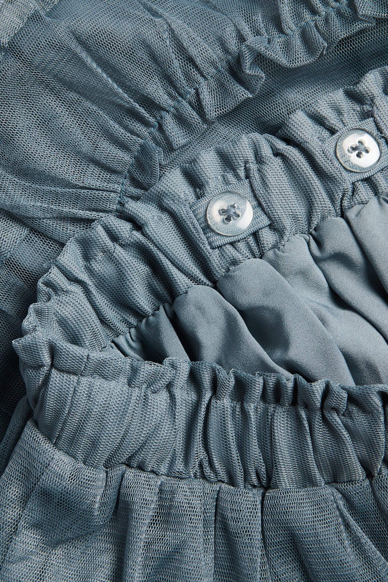 Close-up of a blue mesh skirt with ruffles, an elastic waist, and two visible buttons.
