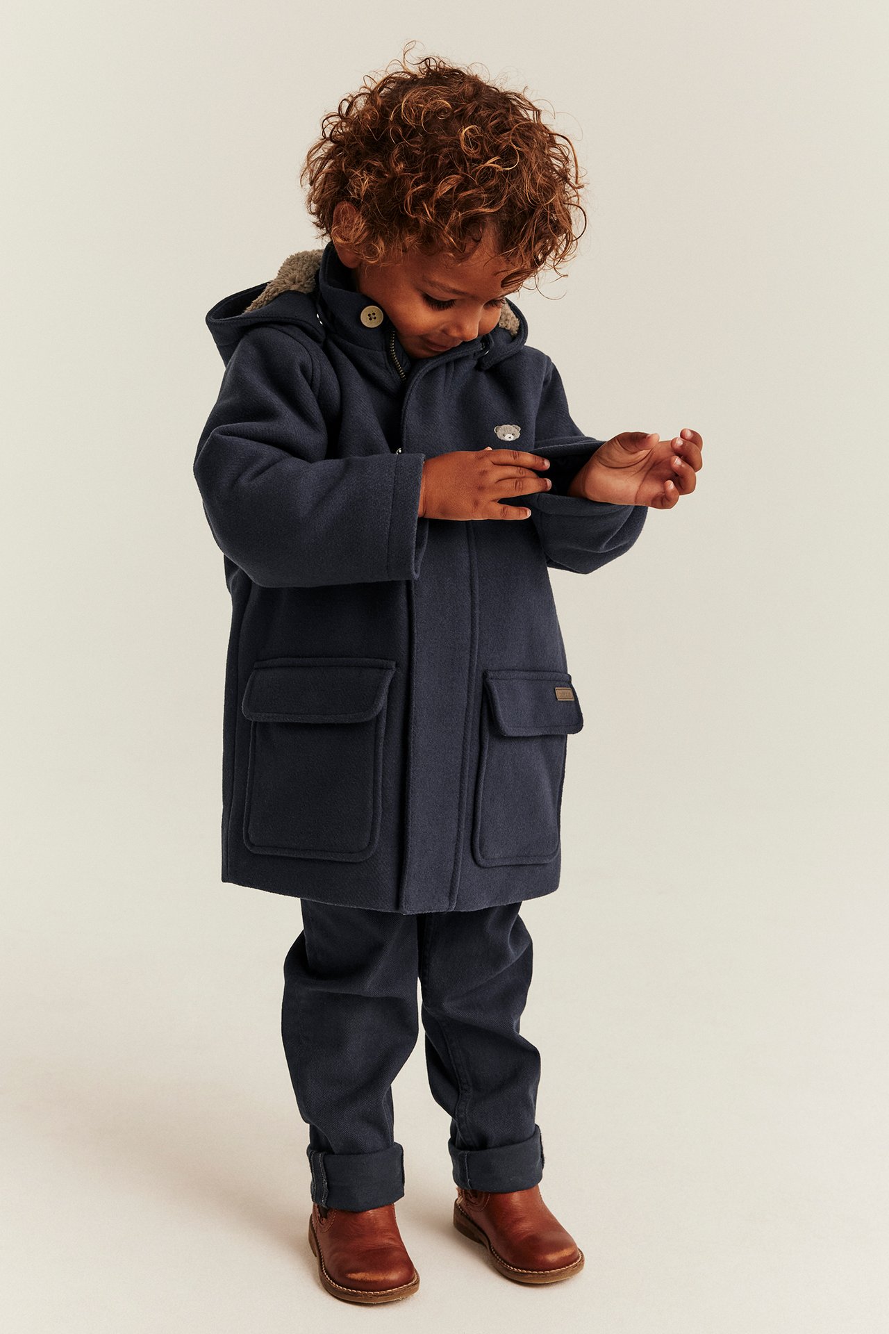 Front view of a kid in a dark blue hooded coat, dark blue pants, and brown shoes.