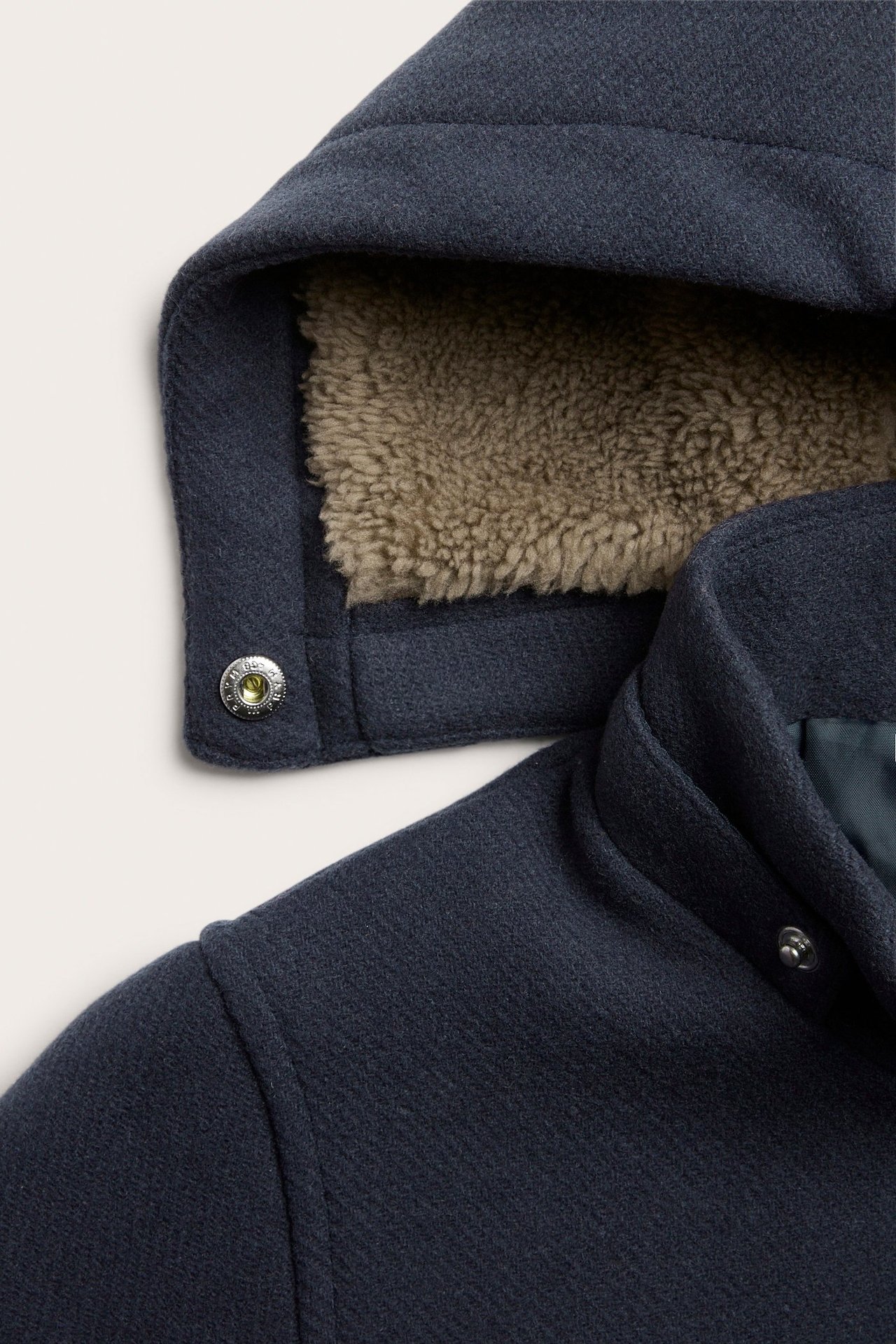 Nahaufnahme eines dunkelblauen Wollmischmantels mit abnehmbarer Kapuze und hellbraunem Teddyfutter.