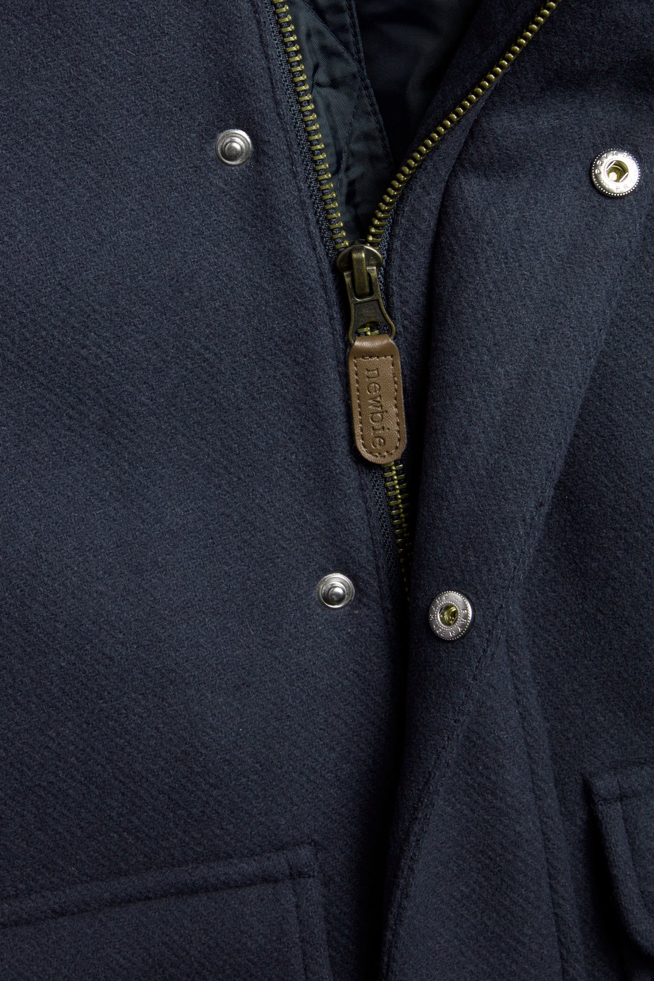 Close-up front view of a dark blue wool blend coat with a zipper, snap buttons, and a pocket.