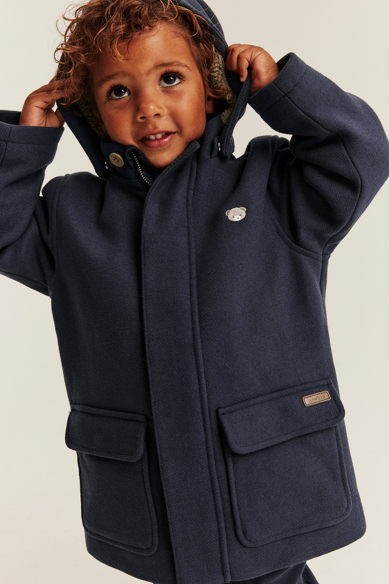 Front view kid's navy blue hooded coat with teddy bear embroidery and two flap pockets.
