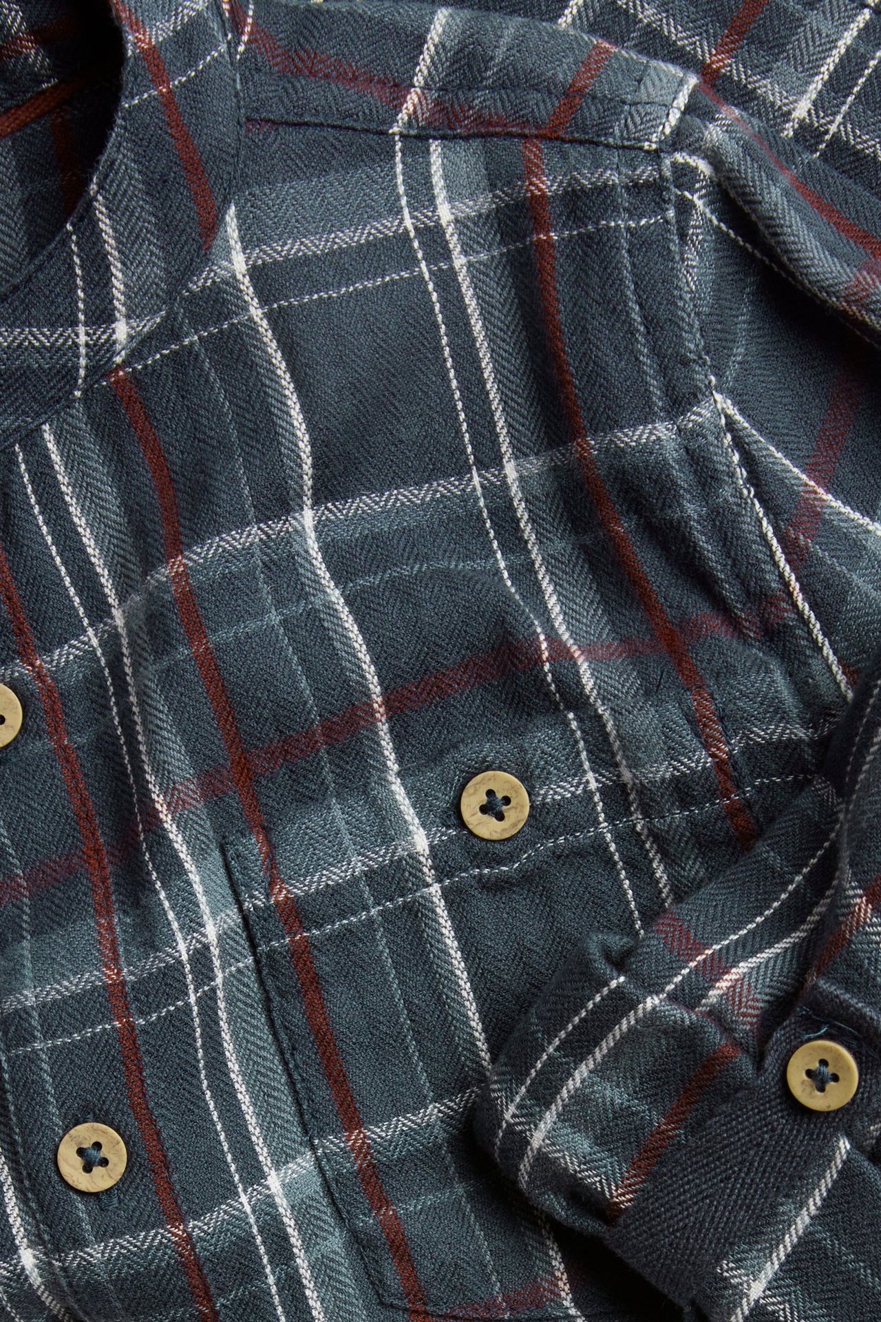 Nahaufnahme eines dunkelblauen karierten Hemdes aus gebürsteter Baumwolle mit Brusttasche und Holzknöpfen.