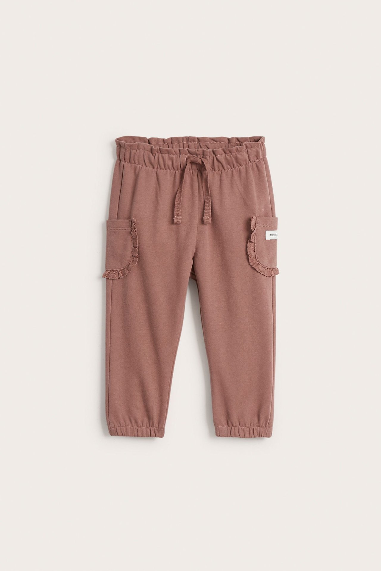 Vorderansicht: Dunkelrosa Baby-Jogginghose aus Baumwolle mit elastischem Kordelzugbund und Rüschenspitzentaschen.