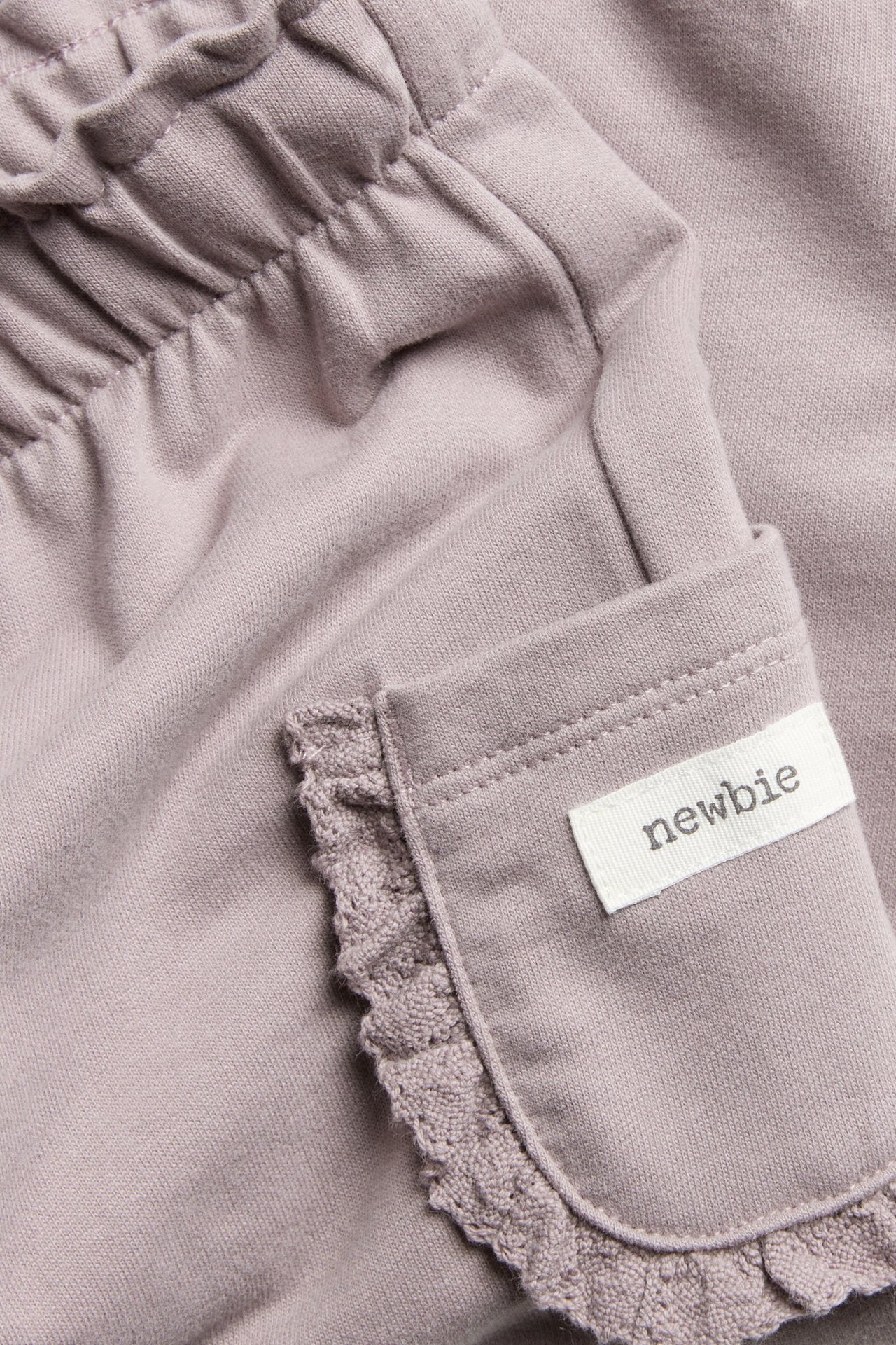 Nahaufnahme von helllila Baumwoll-Jogginghose mit Gummizugbund und spitzenbesetzter Tasche mit "newbie"-Etikett.