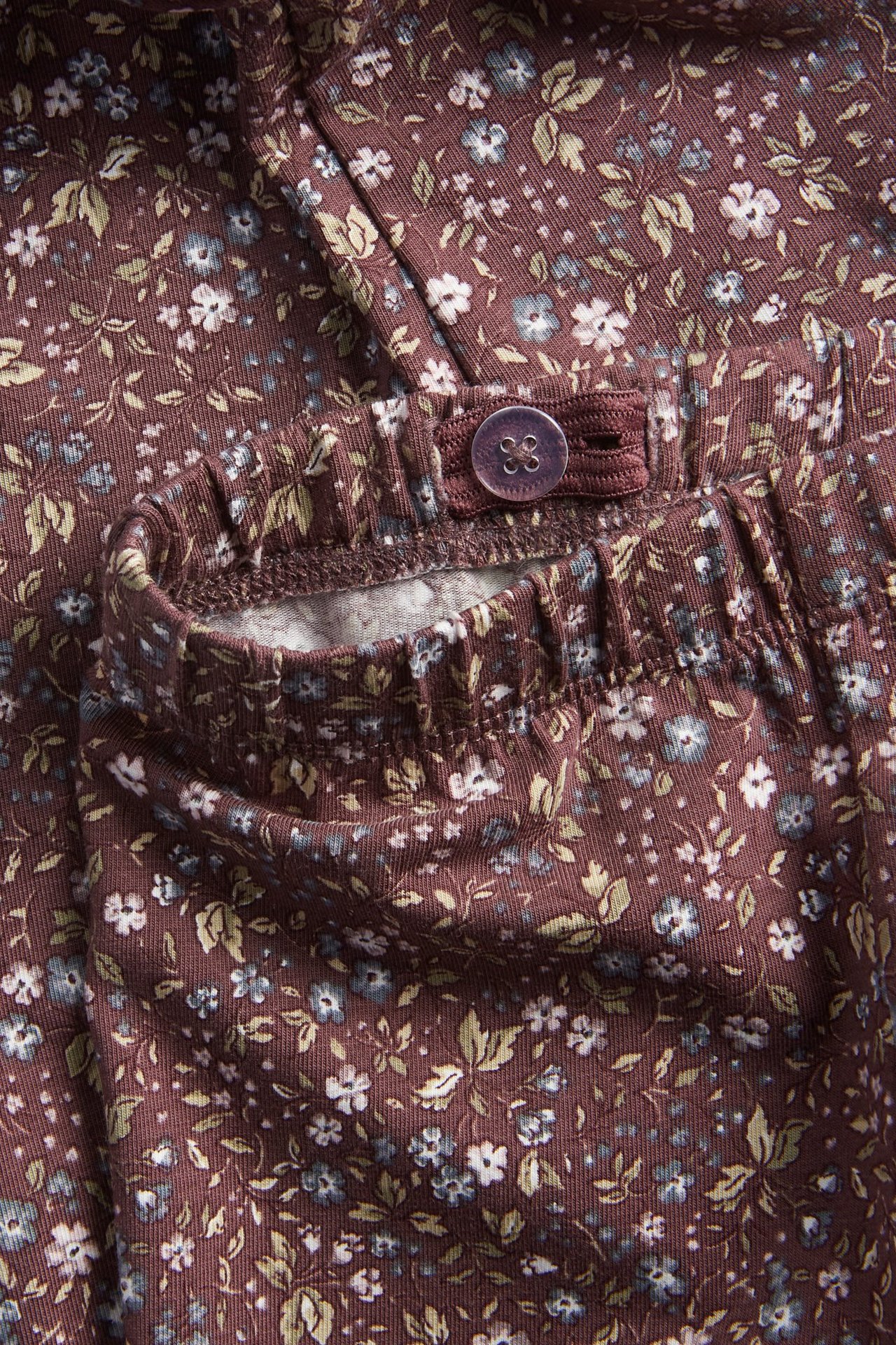 Nahaufnahme von dunkel pflaumenfarbenen floralen Leggings mit verstellbarem Gummibund und Knopf.