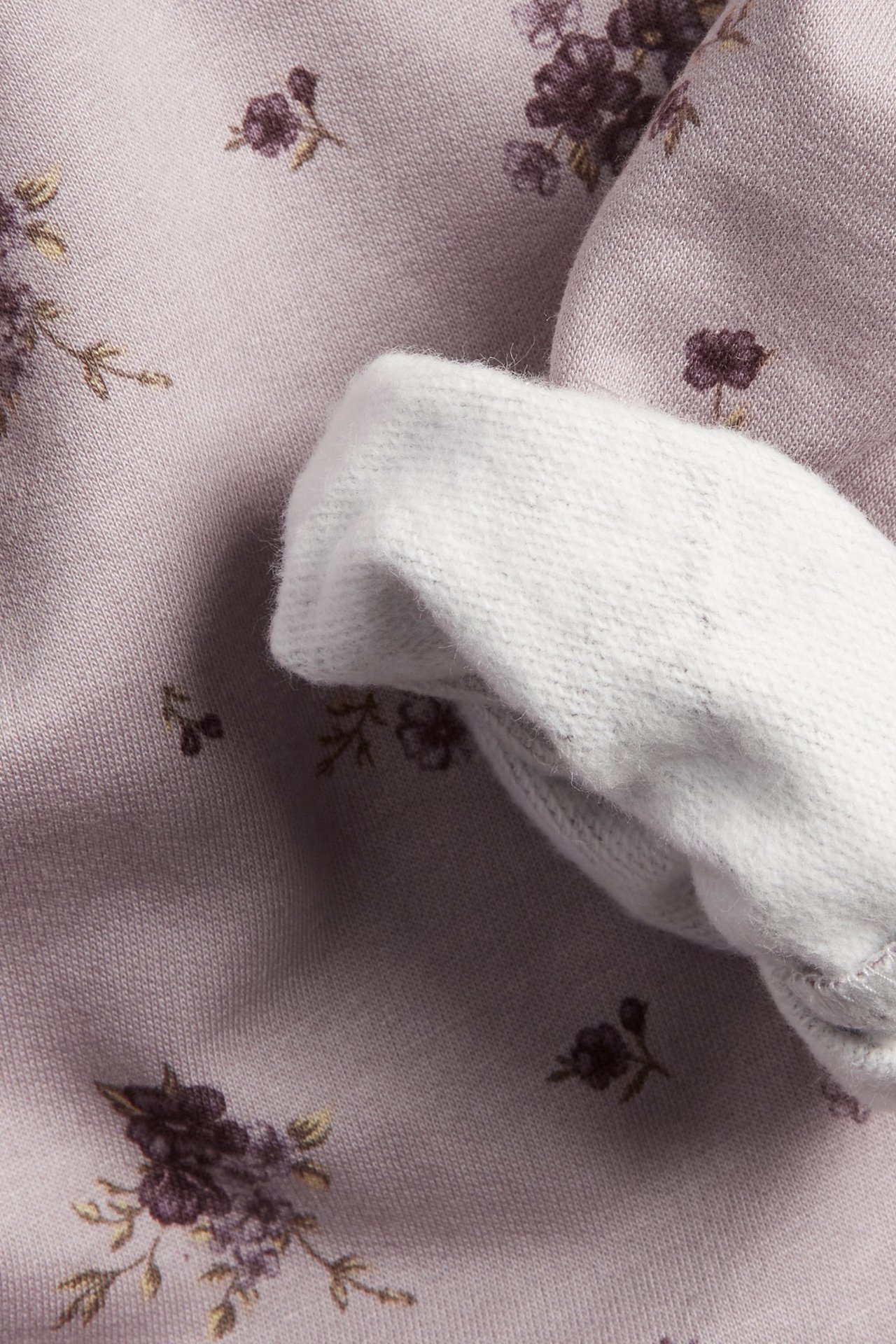Nahaufnahme eines helllila geblümten Baumwoll-Sweatshirts mit weißem geripptem Ärmelbündchen.