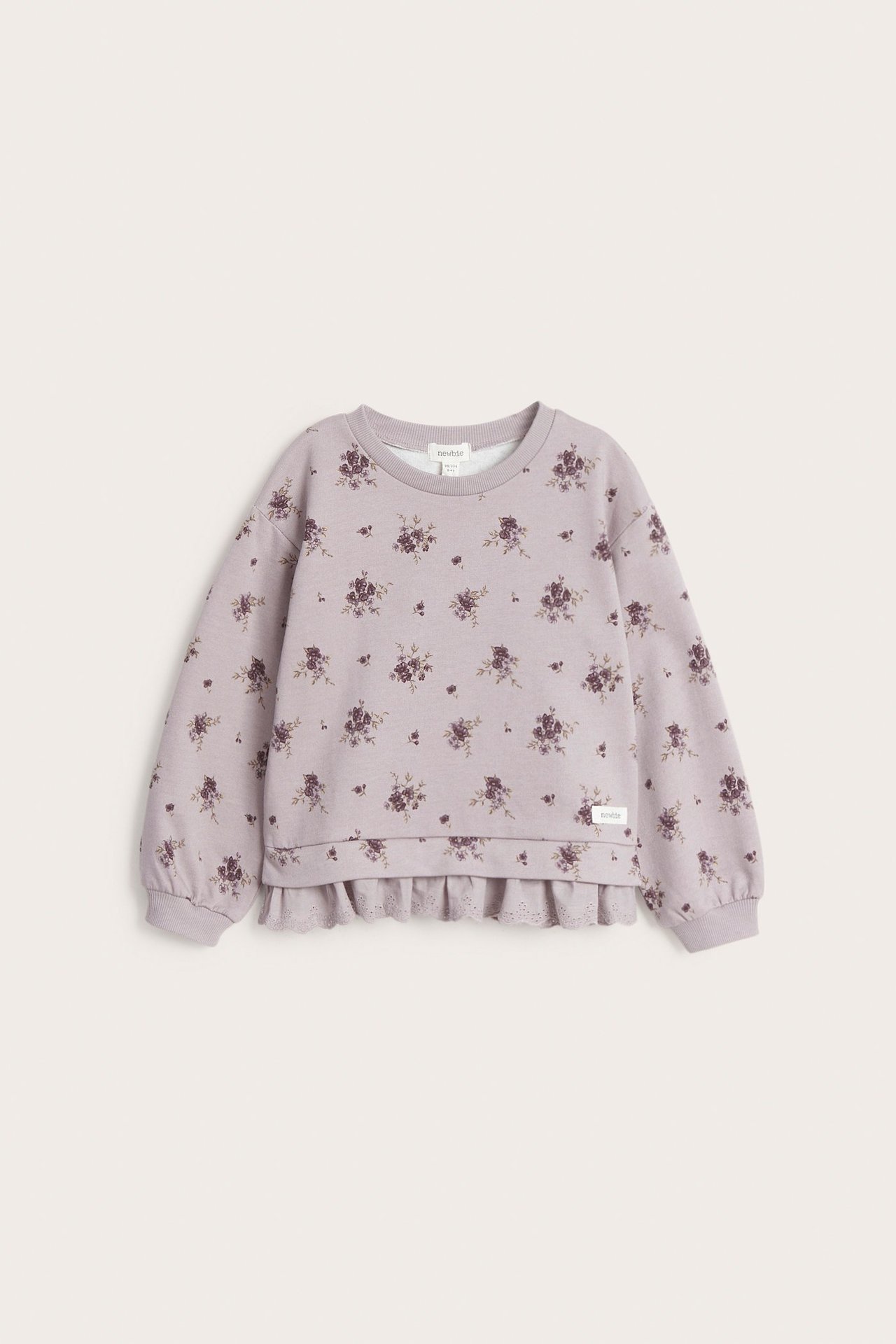 Vorderansicht eines helllila Kinder-Sweatshirts mit Blumenmuster, Spitzenrüsche am Saum und Rippbündchen.