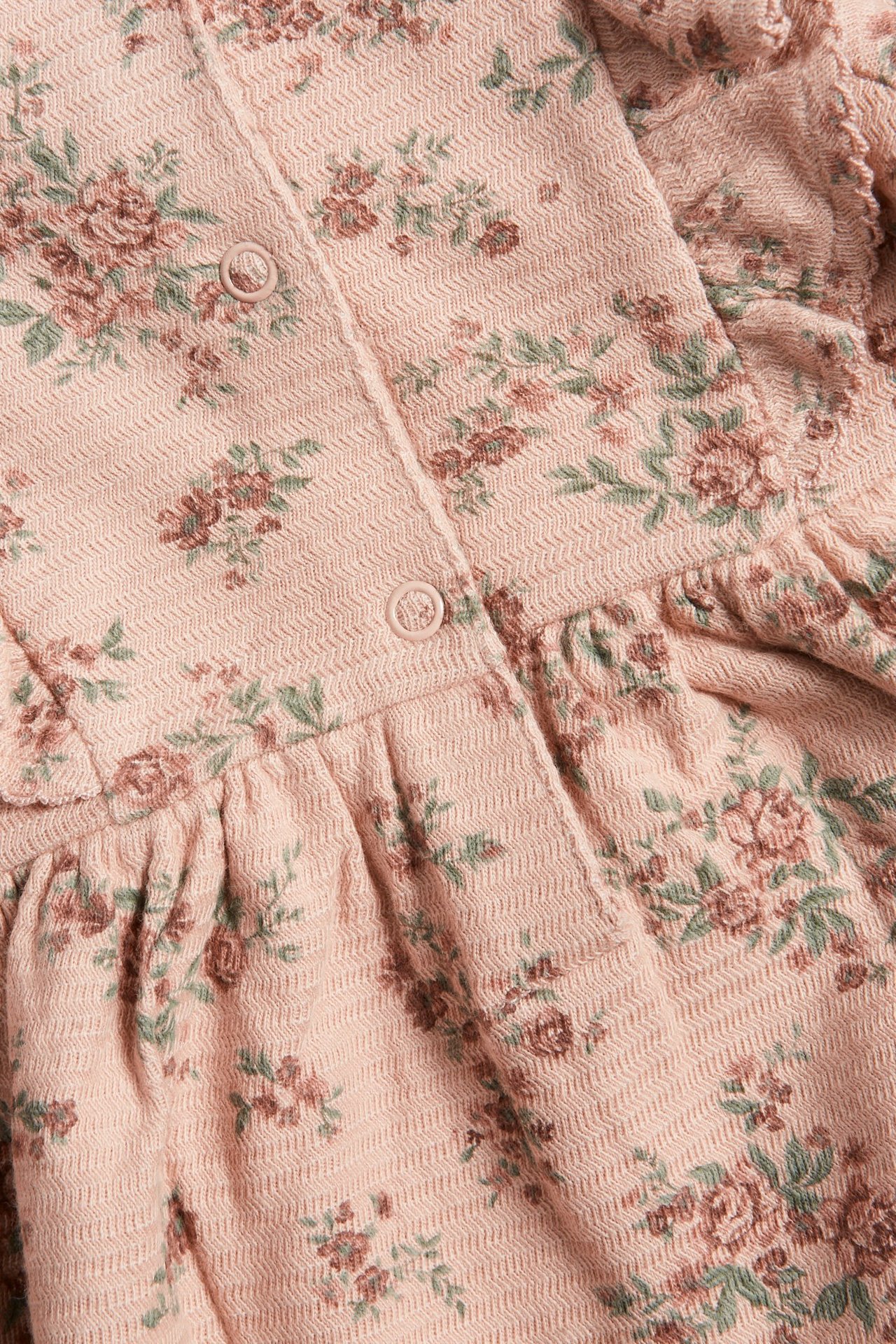 Nahaufnahme eines rosa geblümten Struktur-Jerseykleides mit braunen und grünen Blumen und Druckknöpfen.
