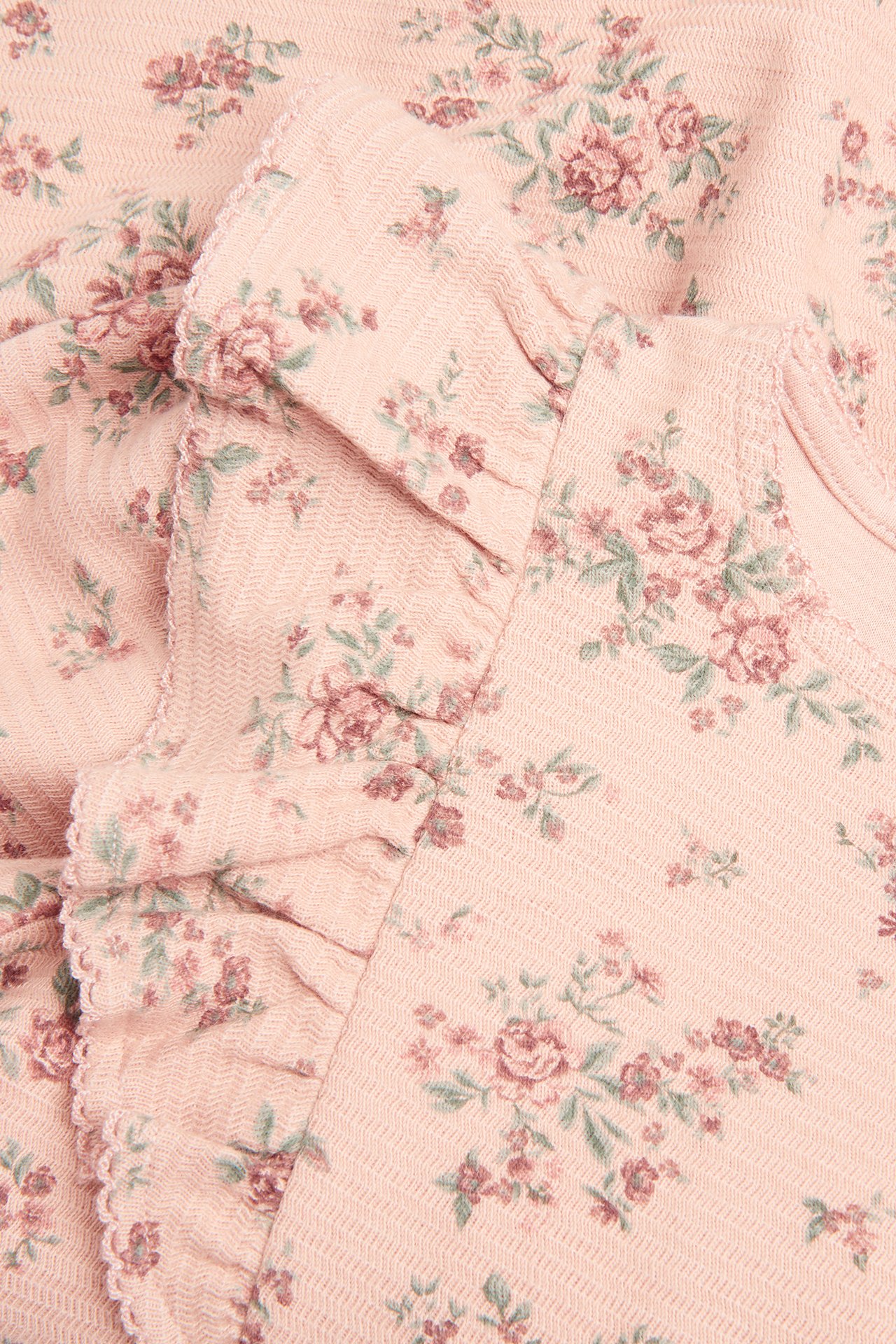 Nahaufnahme eines rosa geblümten Strukturjersey-Kleides mit Rüschen.