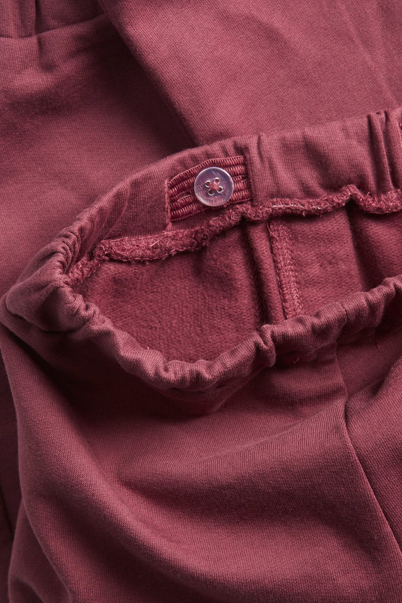 Close-up of wine red cotton jogging pants with an adjustable elastic waistband and button.