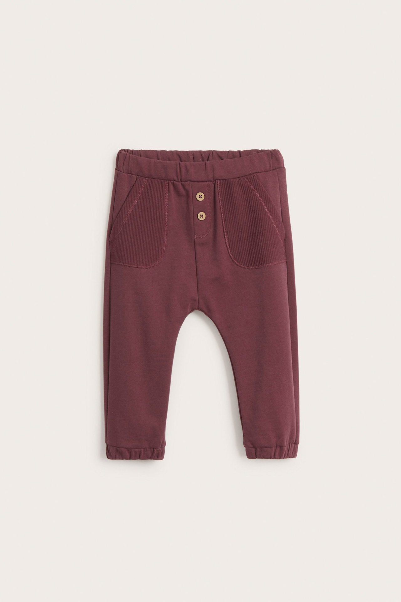 Front view of kid's wine red cotton jogging pants with ribbed front pockets and decorative buttons.