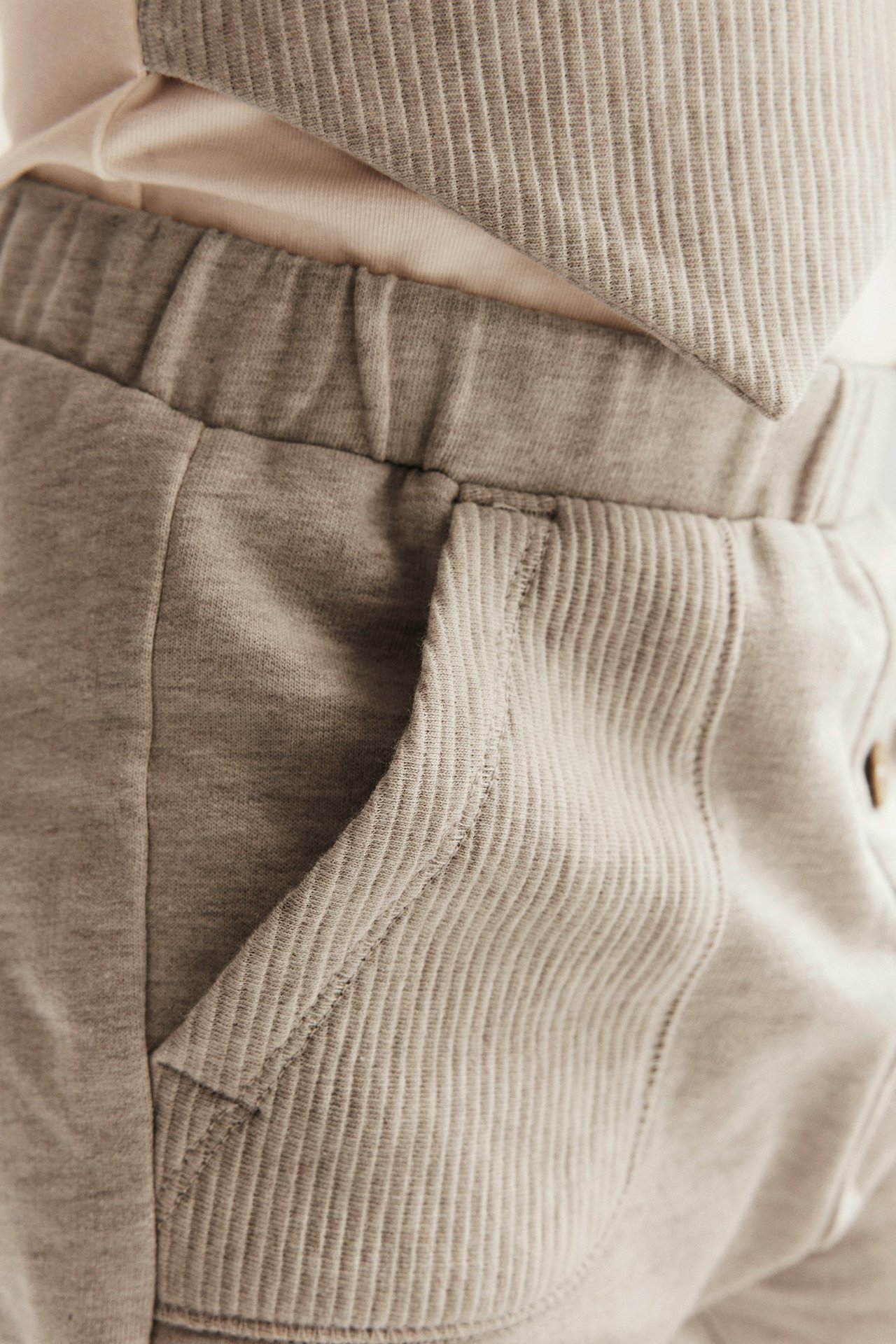 Nahaufnahme von beigemelange Baumwoll-Jogginghose des Kindes mit gerippten Taschen, getragen mit hellem Rippen-Top.