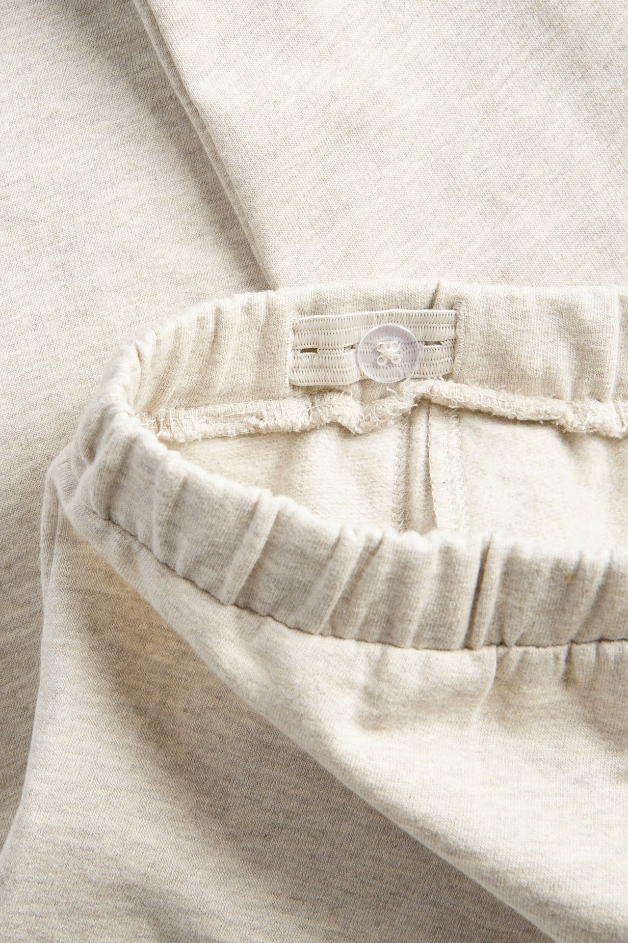 Close-up of beige melange cotton jogging pants with an adjustable elastic waistband and button.