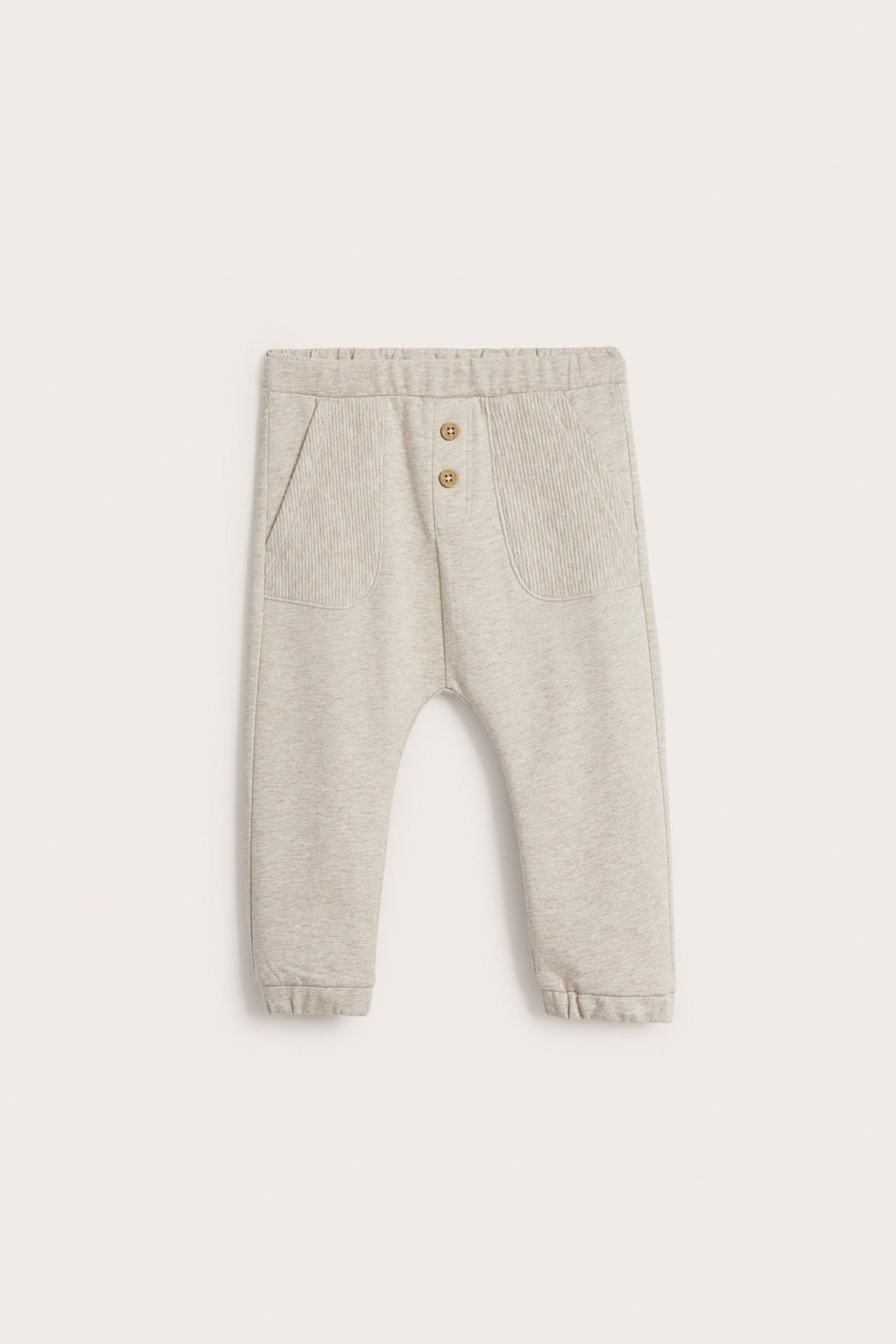 Front view of kid's beige melange cotton jogging pants with ribbed patch pockets and decorative wooden buttons.
