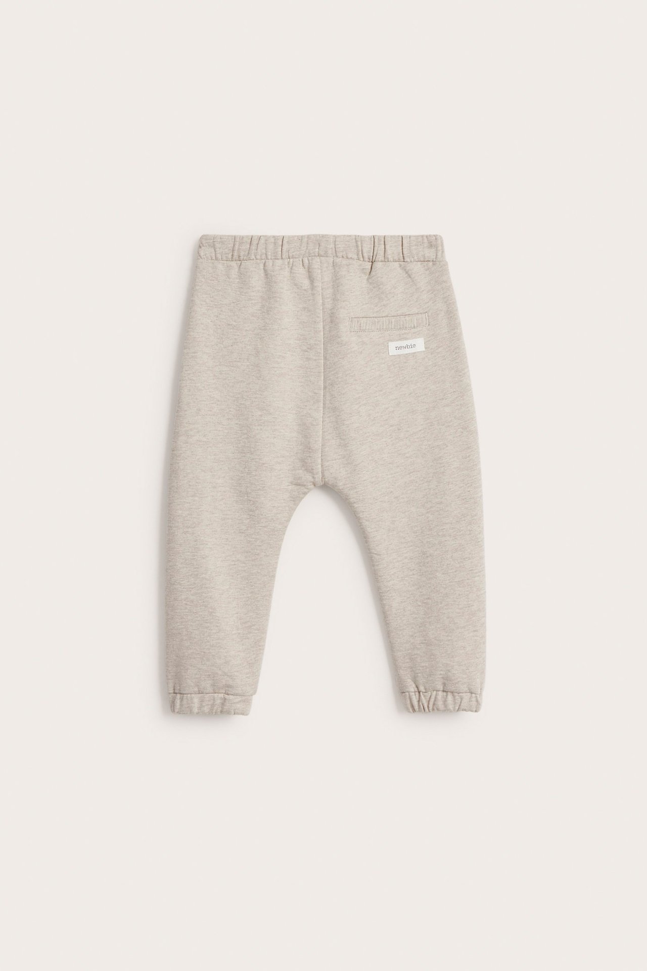 Back view: baby's beige melange cotton jogging pants with elastic waist, ribbed back pocket, and cuffs.