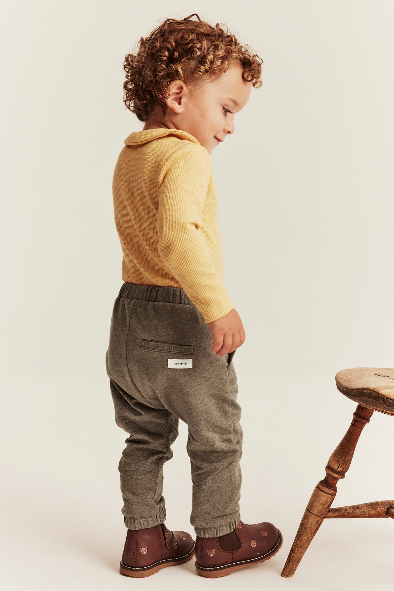 Side view of kid wearing grey joggers, a yellow ribbed polo, and brown embroidered boots.