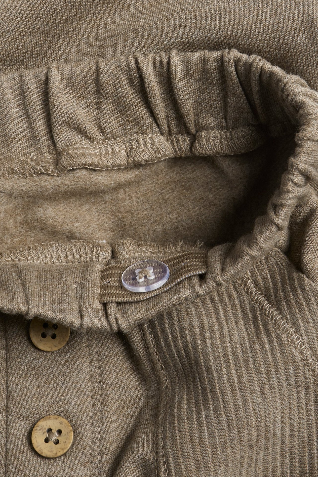 Close-up of brown melange cotton jogging pants, elastic waistband, adjustable inner elastic, decorative buttons.