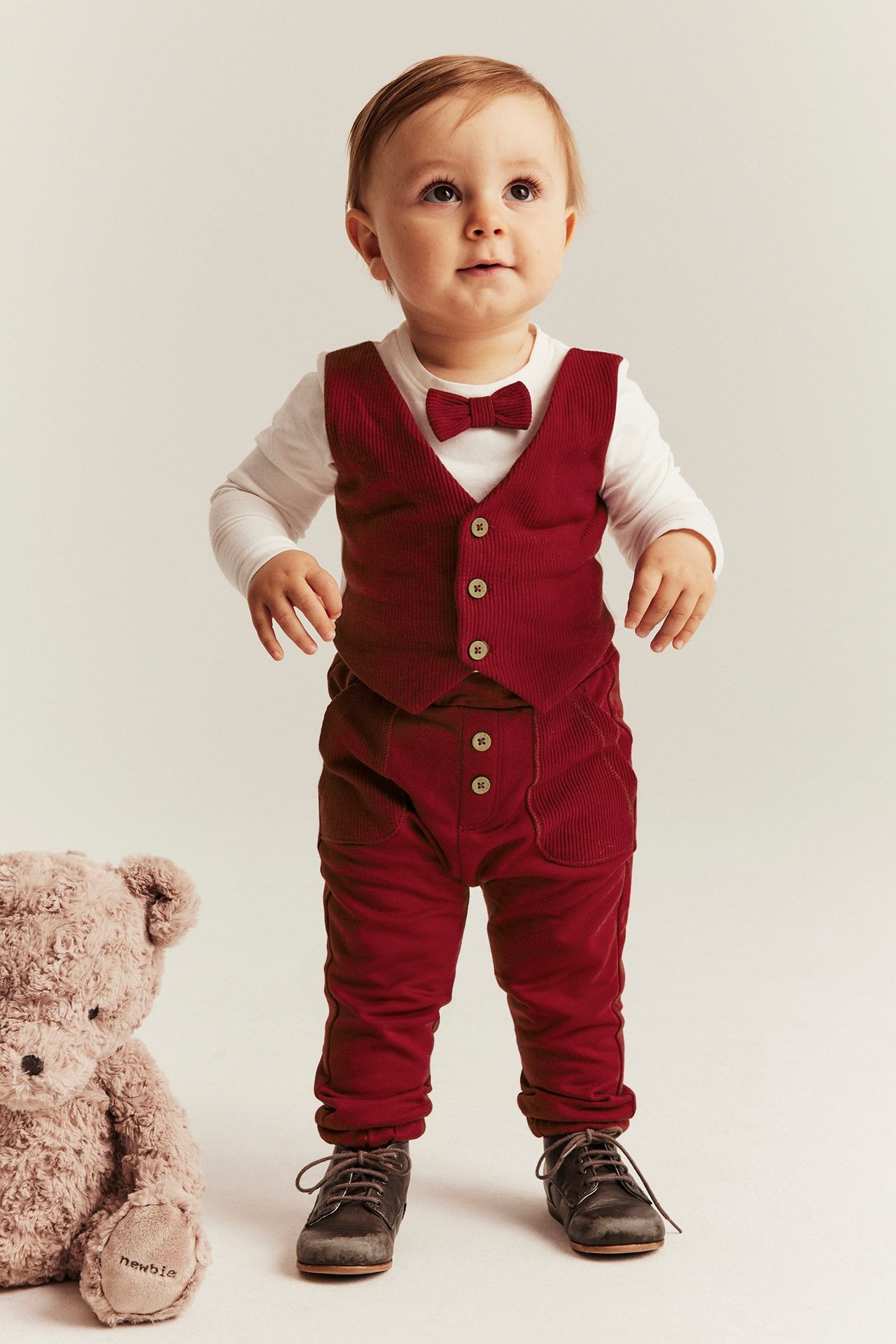 Kid wearing red joggers with front buttons, elastic waist, cuffed legs, and front pockets.