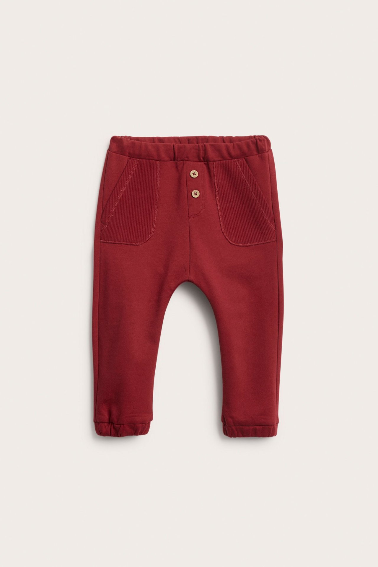 Front view of red baby jogging pants with elastic waist, ribbed patch pockets, and two decorative buttons.