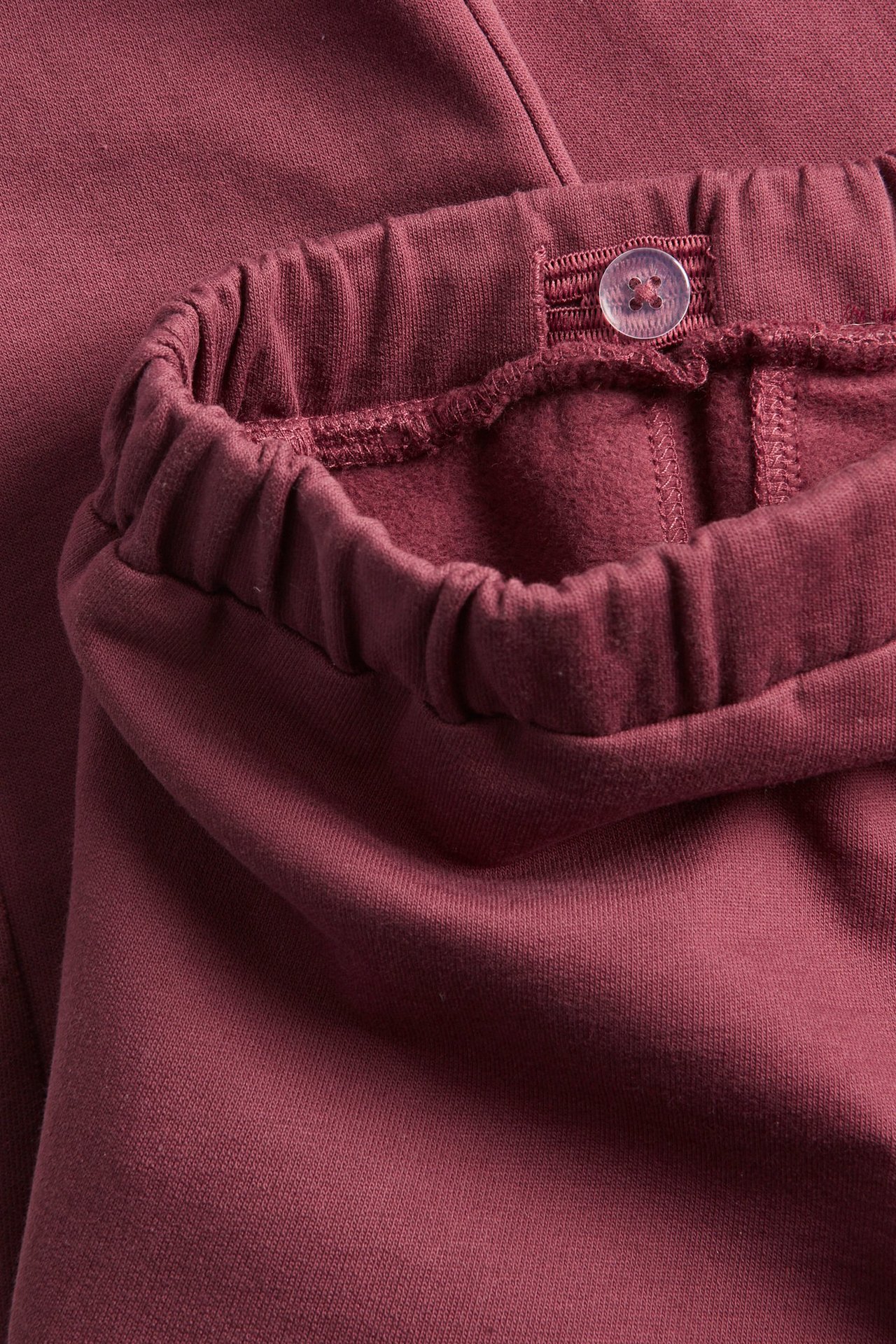 Nahaufnahme von weinroten Baumwoll-Jogginghosen für Kinder, mit elastischem Bund und verstellbarem Knopf.