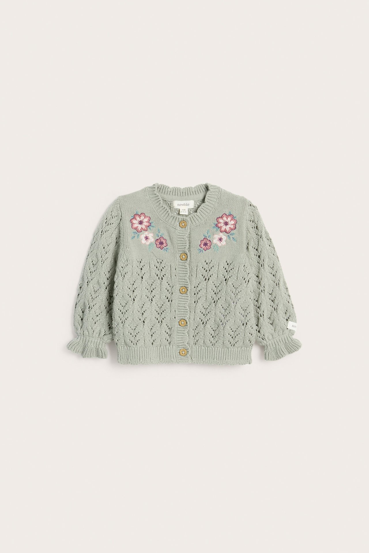 Vorderansicht einer grünen gemusterten Baumwollstrickjacke mit Blumenstickerei, Rüschenbündchen und Holzknöpfen.