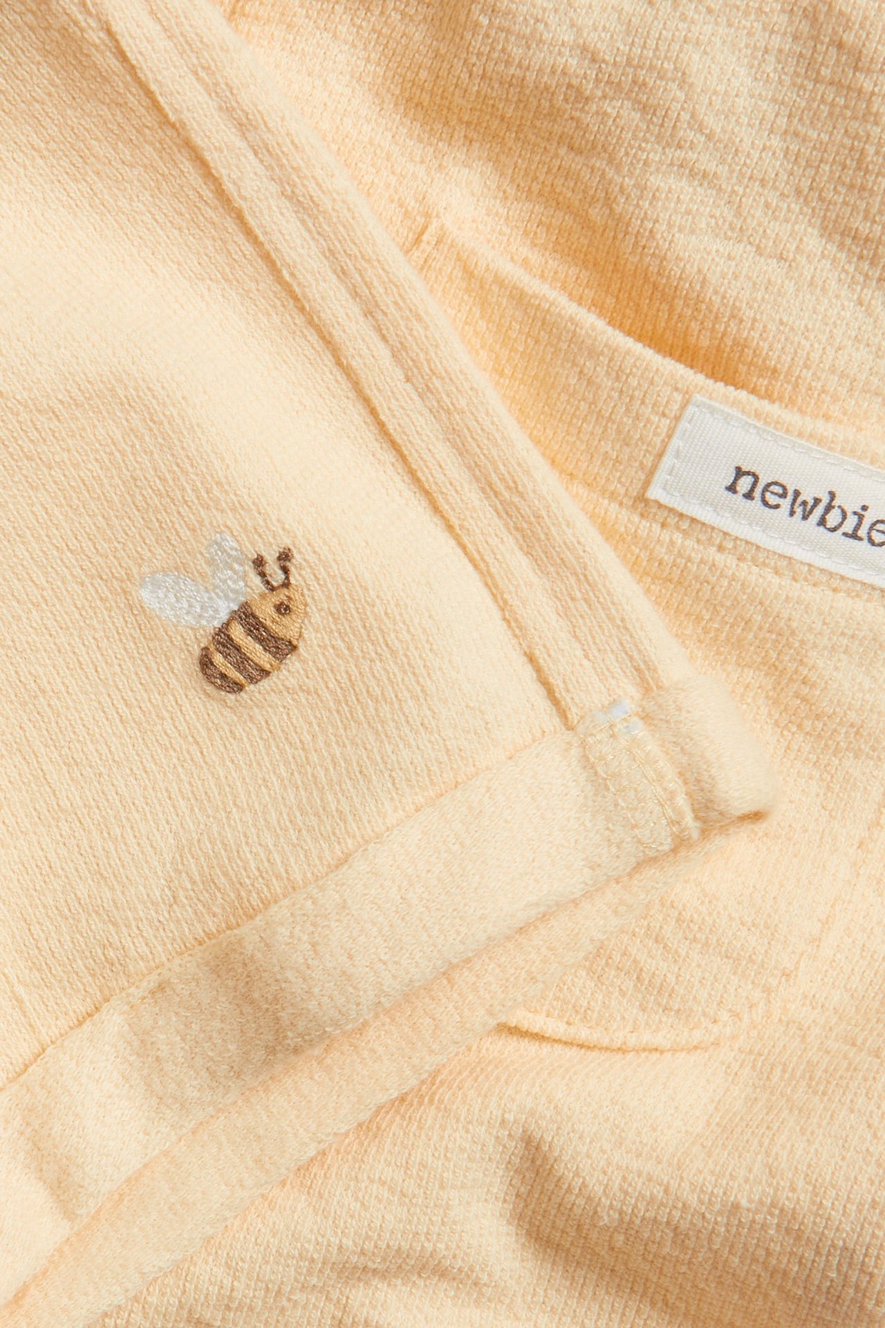 Close-up of yellow cotton shorts with a brown and white bee embroidery and rolled-up cuffs.