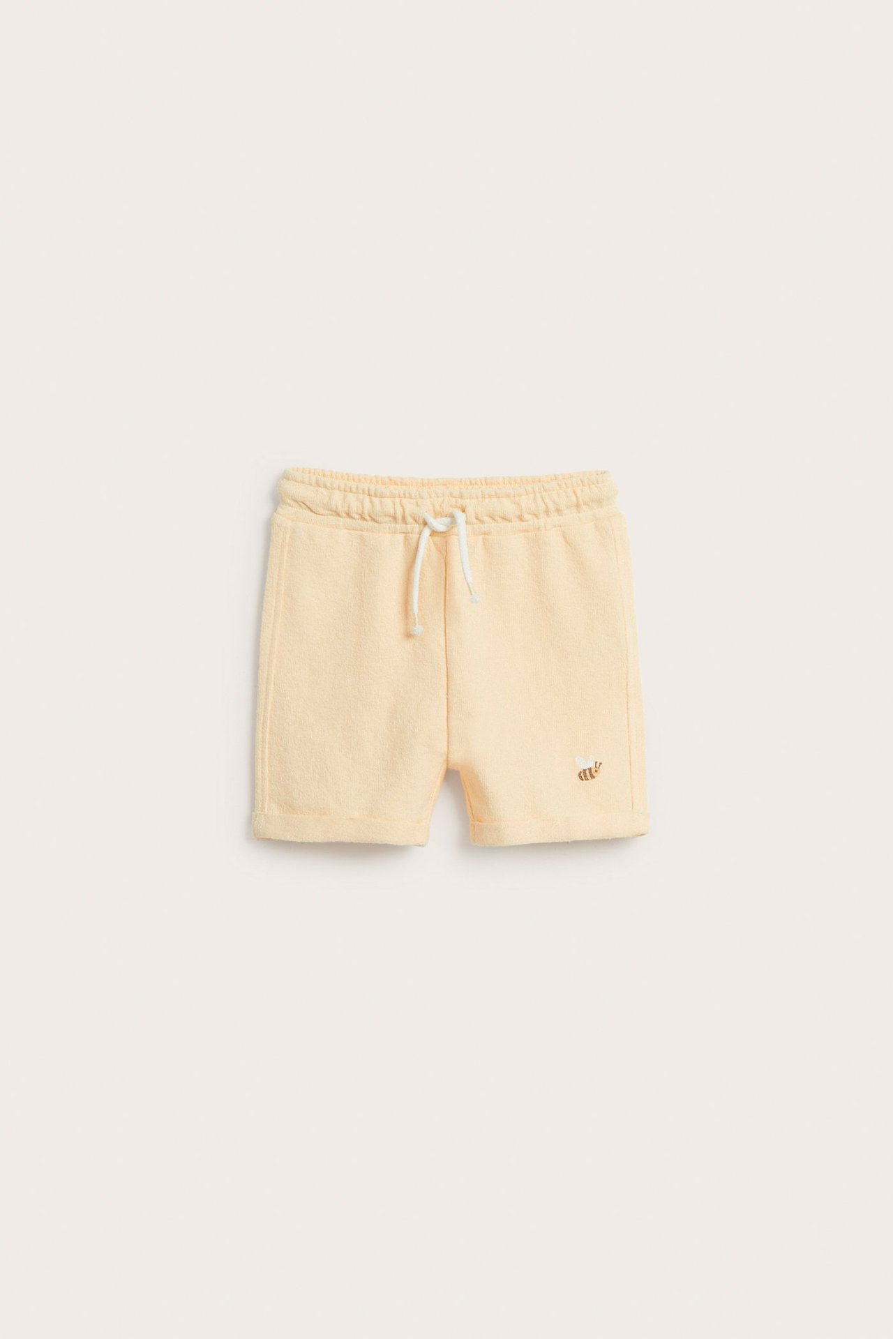 Front view of kid's pale yellow cotton shorts with elastic waist, white drawstring, and small embroidery.