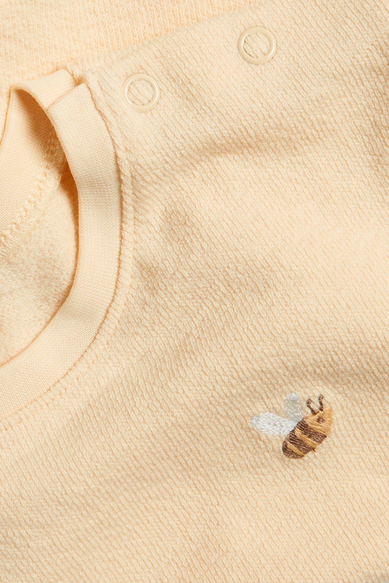 Close-up of a yellow cotton short-sleeved t-shirt with shoulder snap buttons and a bee embroidery.