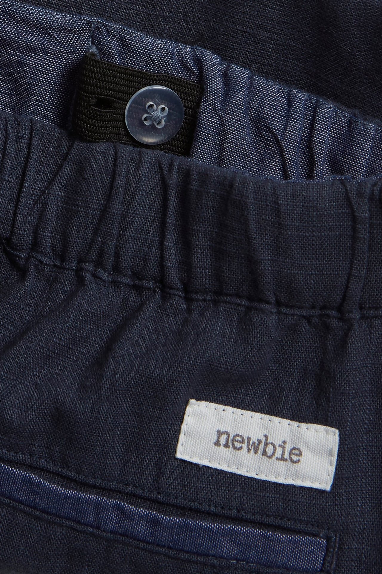 Nahaufnahme von dunkelblauen gewebten Shorts mit elastischem Bund, verstellbarem Innenband, Knopf und 'newbie'-Etikett.