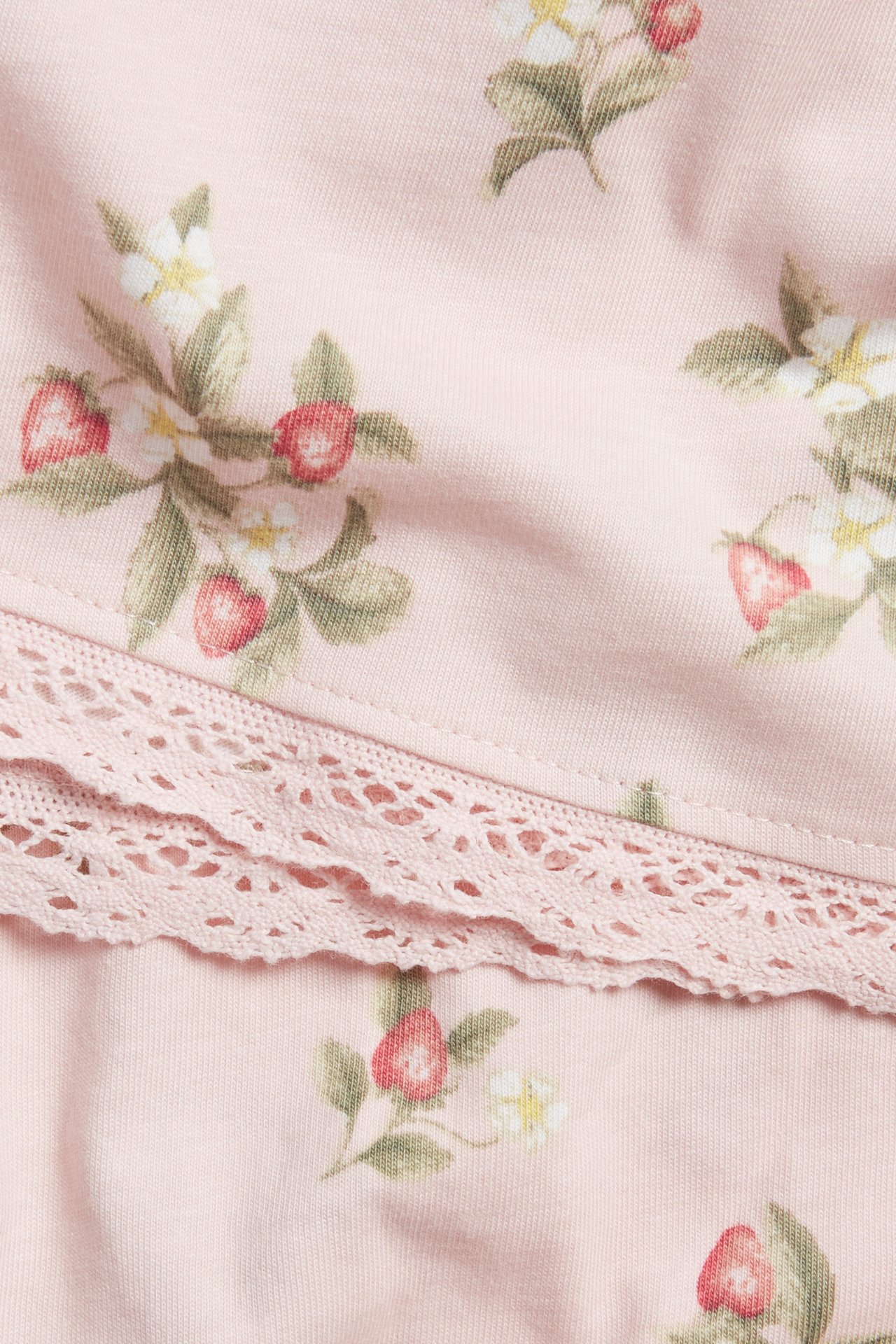 Close-up of a light pink cotton jersey dress with a strawberry and flower pattern and lace trim.