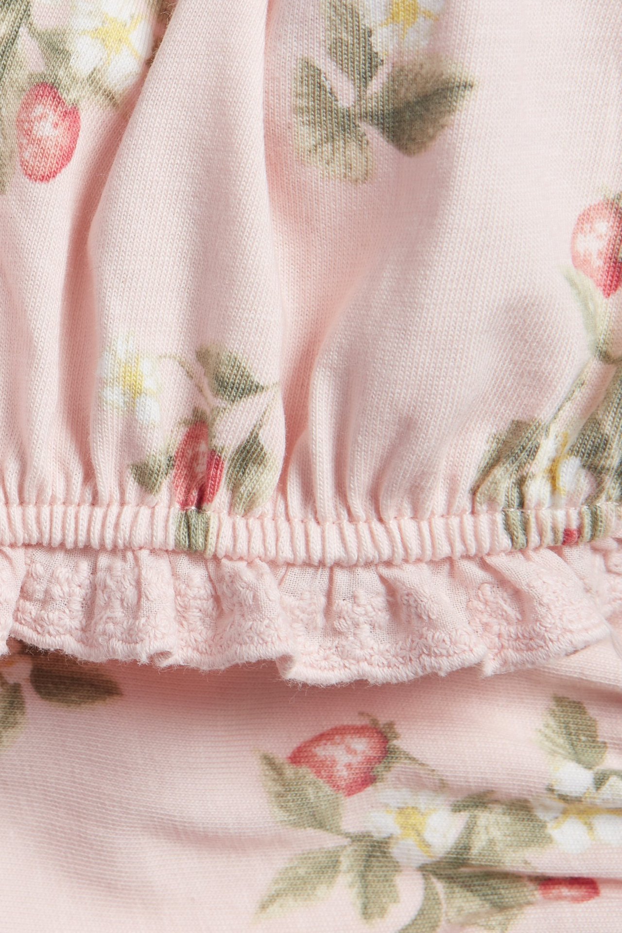 Close-up of light pink jersey shorts with a strawberry and flower pattern, featuring an elasticated waist and ruffle trim.