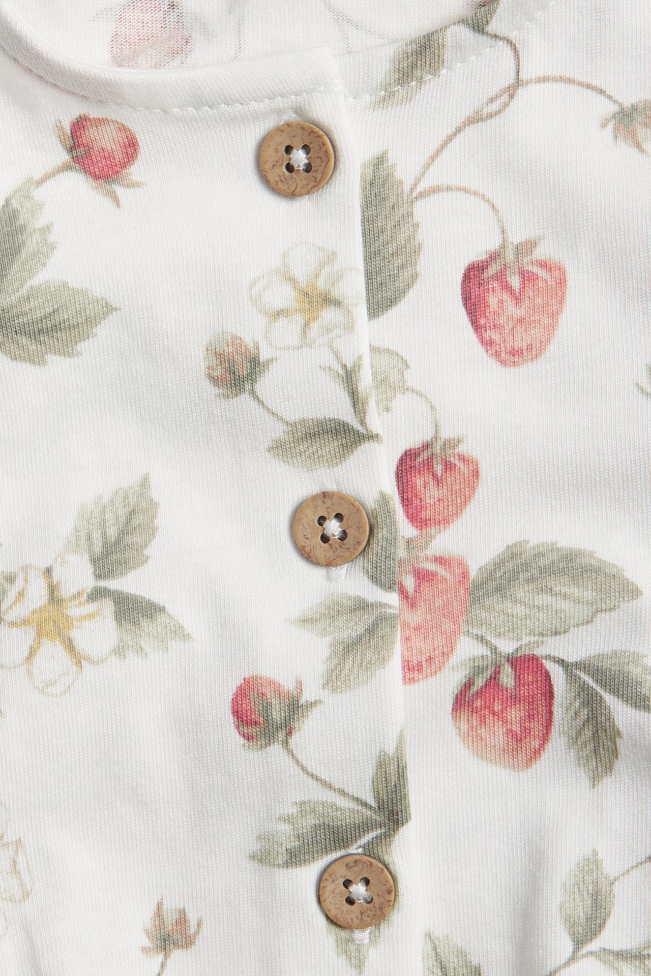 Close-up of an offwhite jersey jumpsuit with a red strawberry pattern and visible wooden buttons.