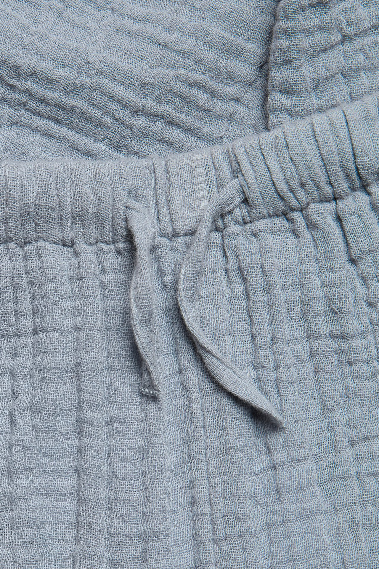 Close-up of light blue woven cotton trousers with an elasticated drawstring waist.