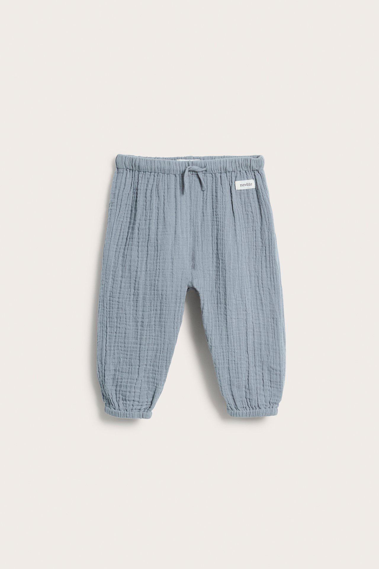 Front view of light blue woven cotton baby pants with an elastic waist, drawstring, and elastic cuffs.