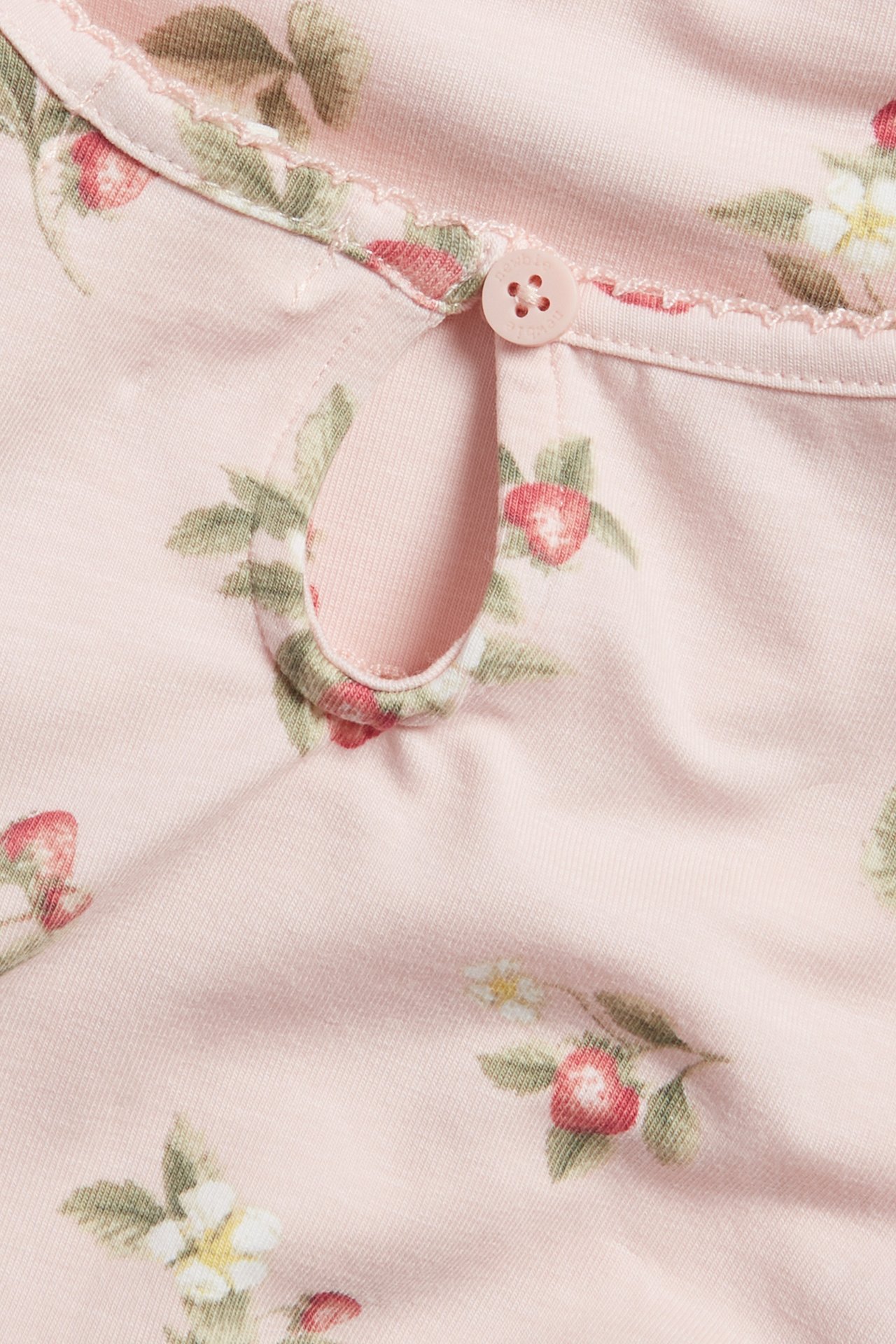 Close-up of a light pink baby's short-sleeved bodysuit with strawberry print, picot trim, and button.