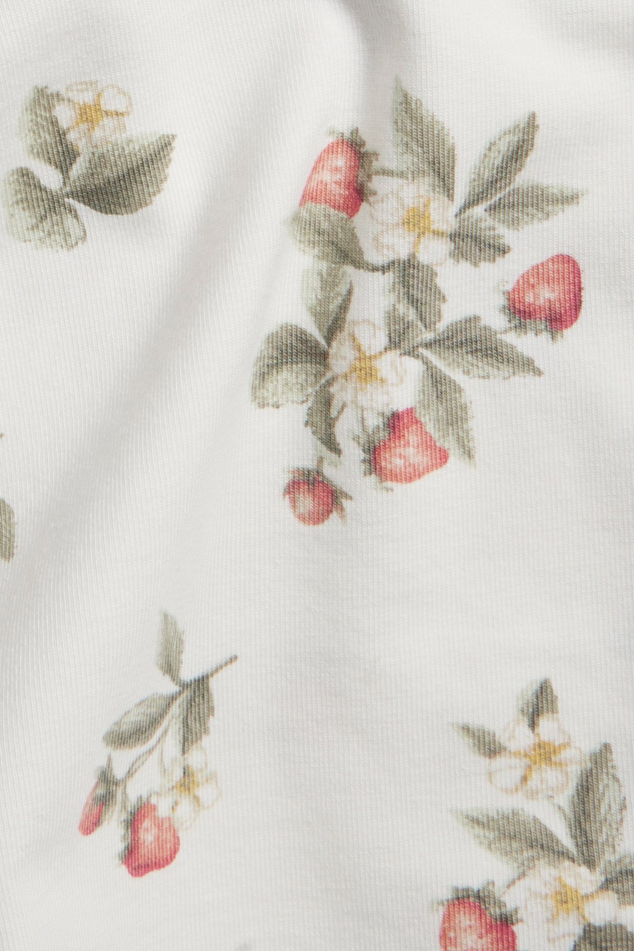 Nahaufnahme von cremefarbenem Baby-Body-Stoff mit rotem Erdbeer- und weißem Blumenmuster.