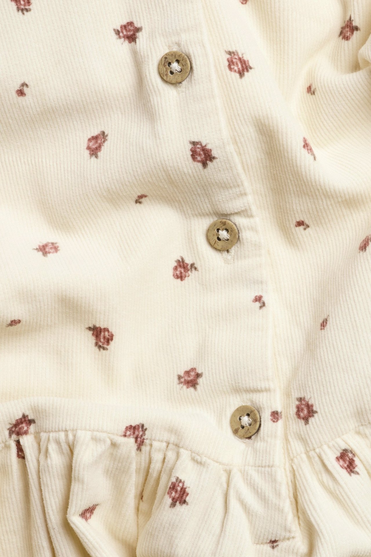 Close-up of a light beige corduroy dress with small reddish-brown floral print and three round buttons.
